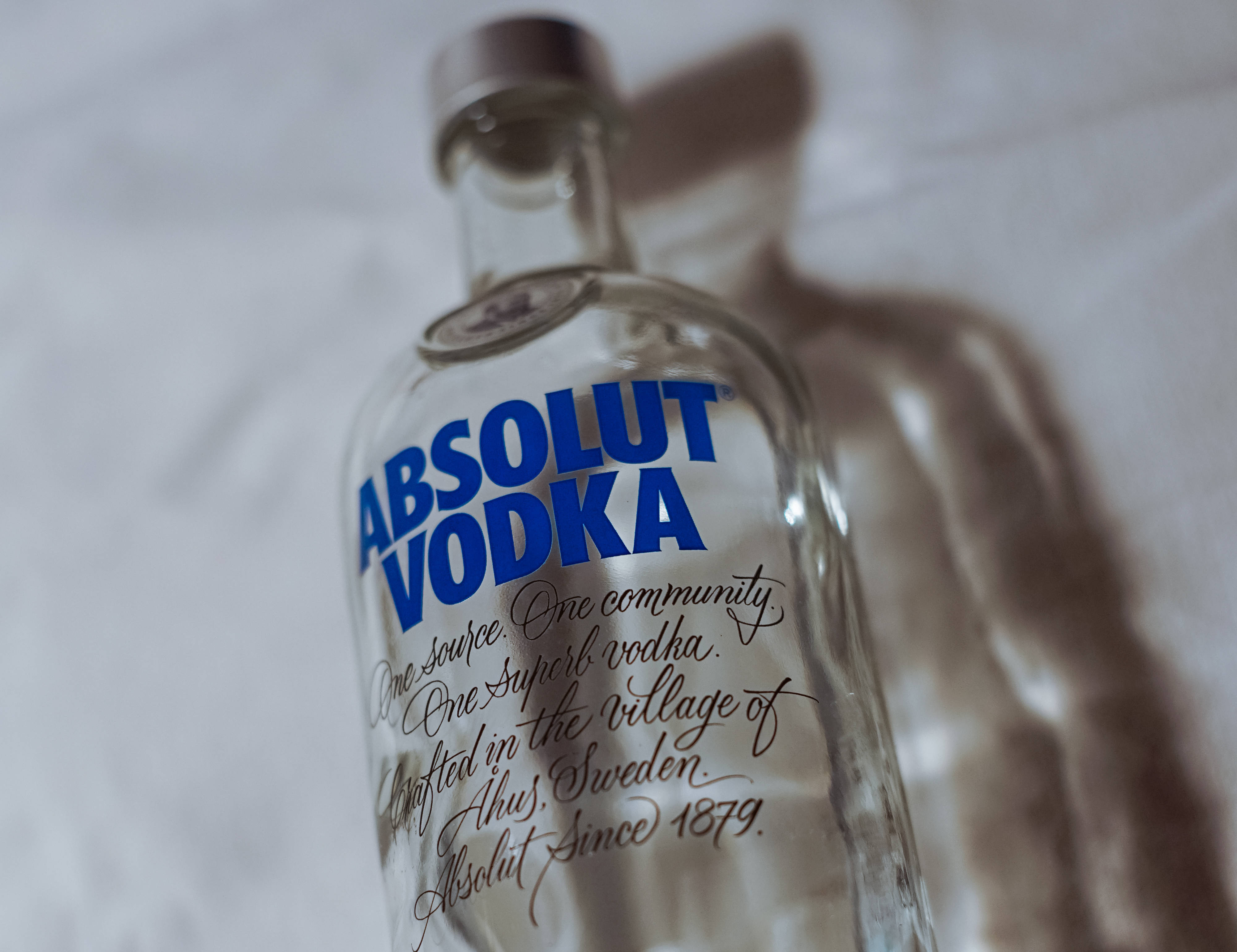 Vodka 桌布 壁紙 — 一個帶有藍色品牌的透明Absolut Vodka酒瓶放在白色布料表面上，投下柔和陰影。