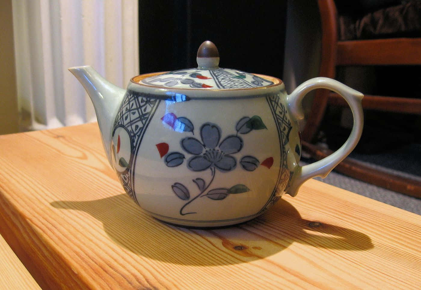 Ceramic 桌布 壁紙 — 一個帶有藍色花卉圖案的陶瓷茶壺放在一張木桌上，沐浴在溫暖的室內光線中。