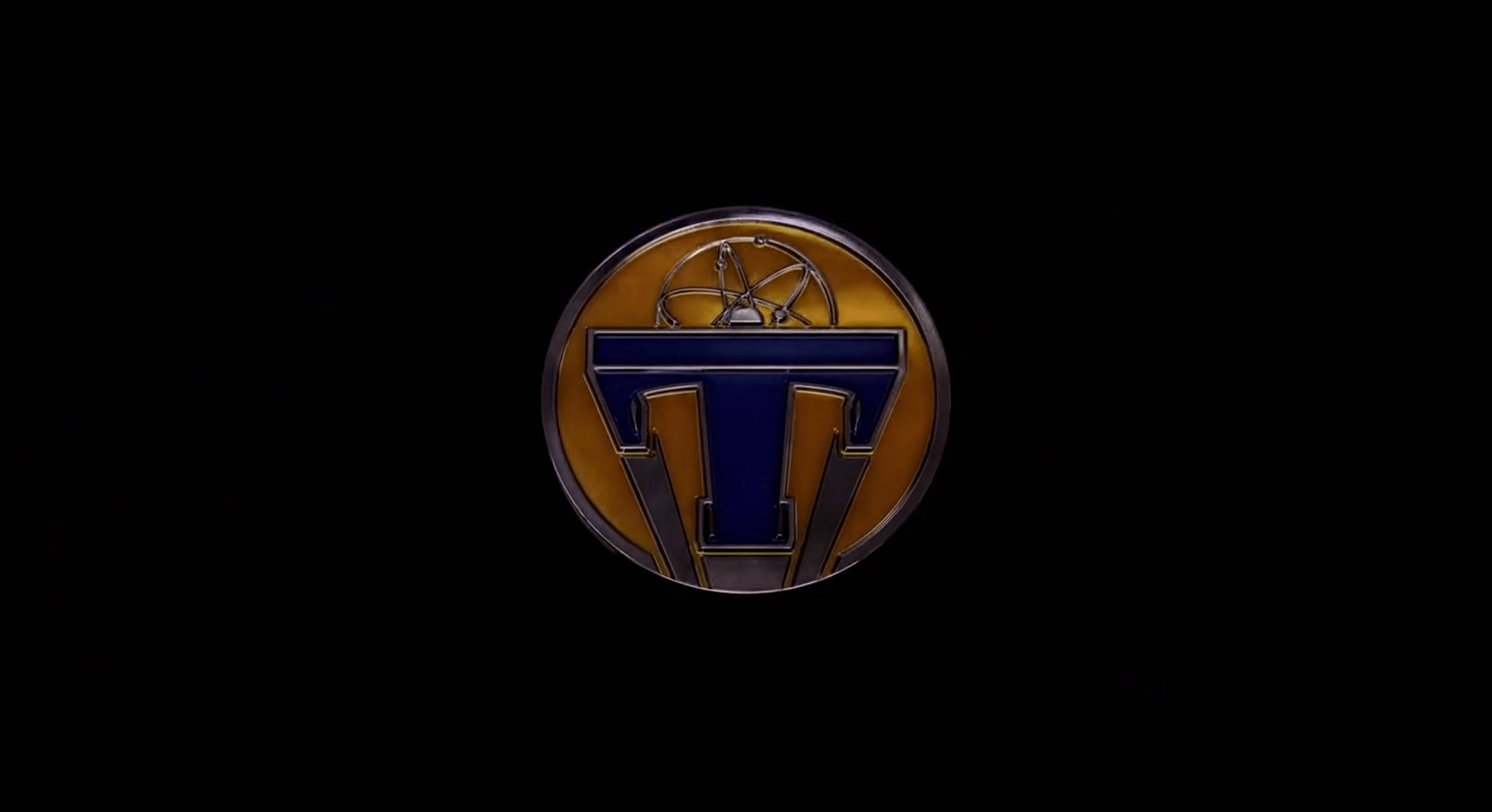 Tomorrowland Movie 桌布 壁紙 — 一個帶有藍色風格化T和地球儀的光澤圓形徽章，置於純黑色背景上。