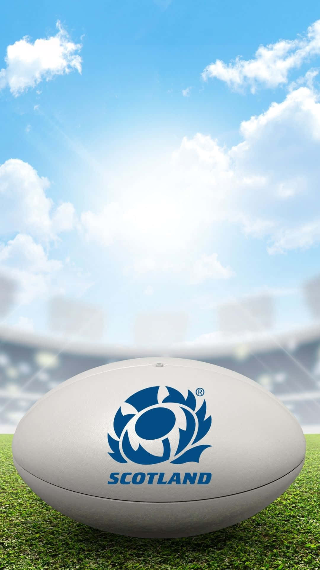 Scotland Rugby 桌布 壁紙 — 一個帶有蘇格蘭藍色薊花標誌的白色橄欖球，放在鮮綠色的草地上，背景是晴朗陽光和蓬鬆雲朵的天空。