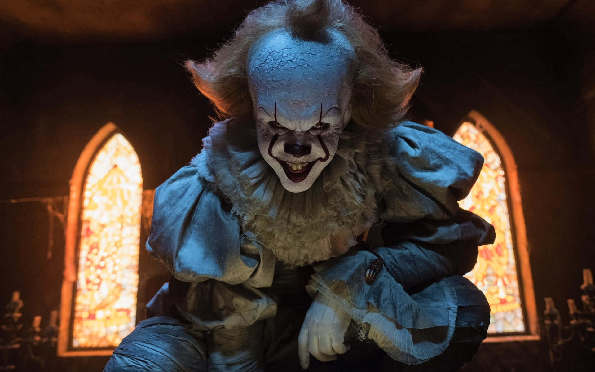 It 2017 桌布 壁紙 — 一個帶有裂紋藍色化妝和狂野頭髮的威脅性小丑蹲在光線昏暗的教堂裡，背後有彩色玻璃窗發光。