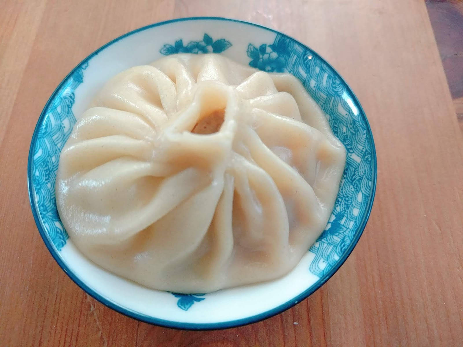 steam 桌布 壁紙 — 一個帶有褶皺麵皮的蒸餃放在藍色花卉碗中，置於木桌上。