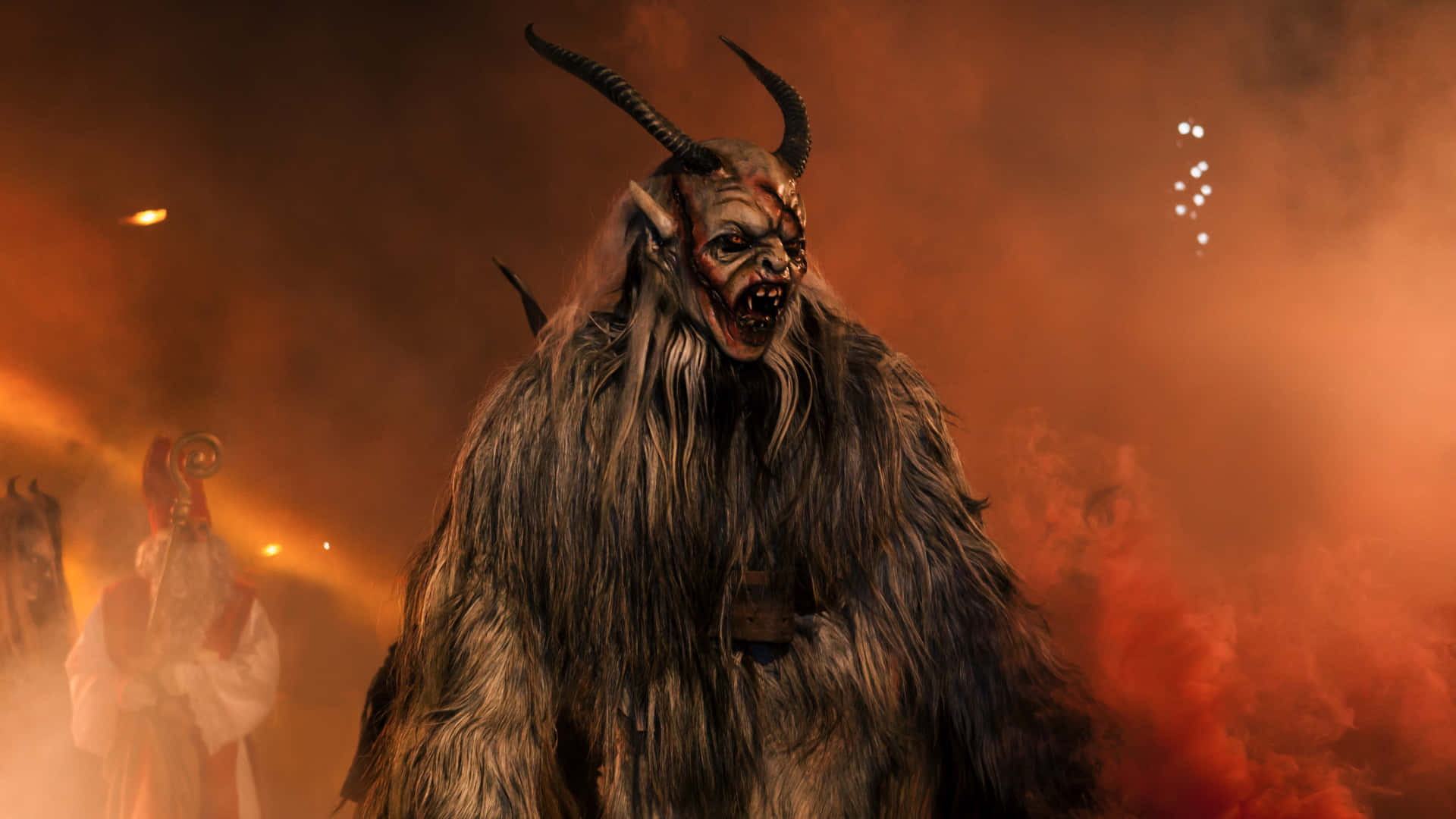 Krampus 桌布 壁紙 — 一個帶有角、毛茸茸、眼睛發光的威脅性惡魔，在舞台燈光下站在火橙色的煙霧中。