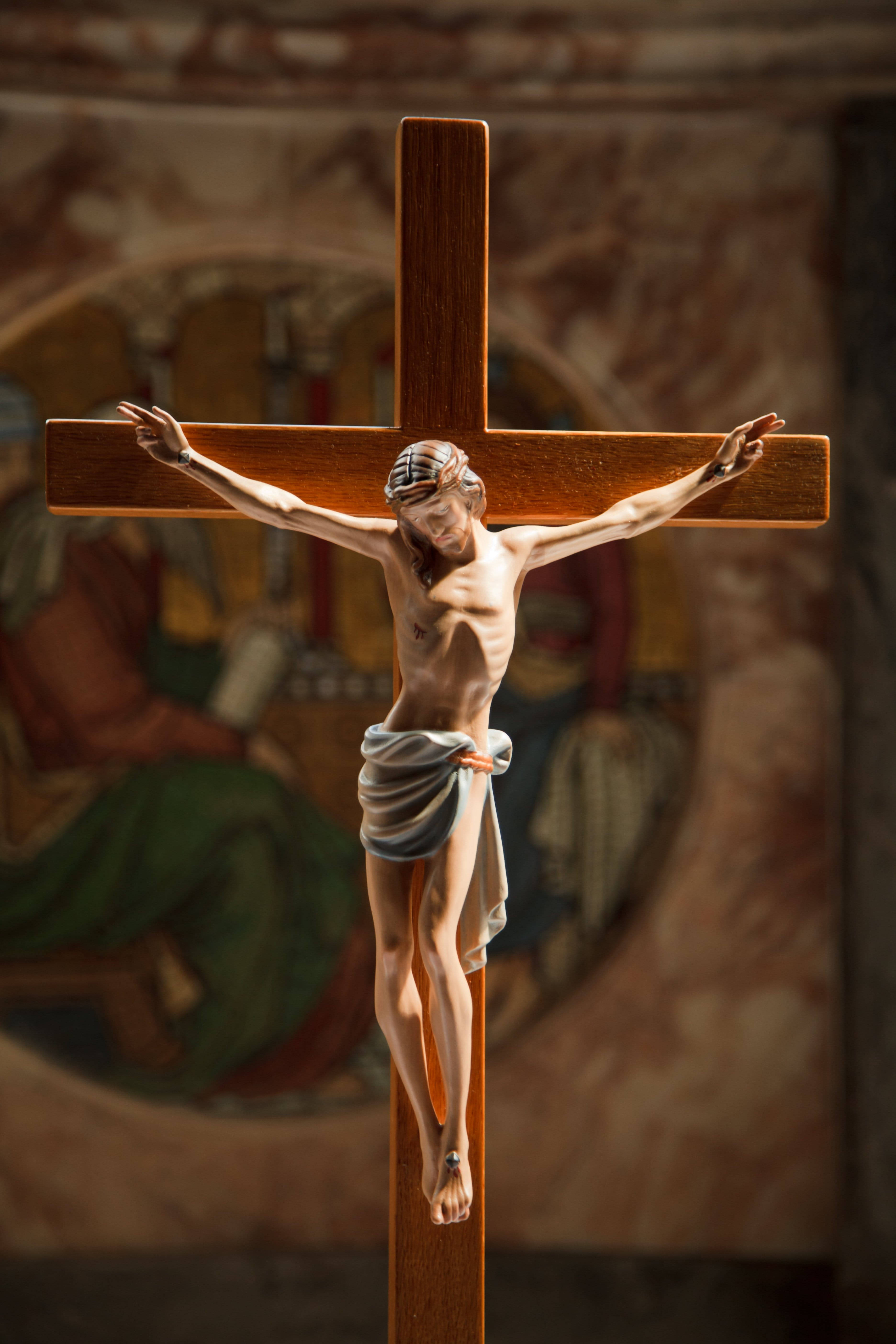 Christ 桌布 壁紙 — 一個帶有詳細耶穌基督像的木製十字架掛在光線柔和、背景有褪色宗教壁畫的教堂中。
