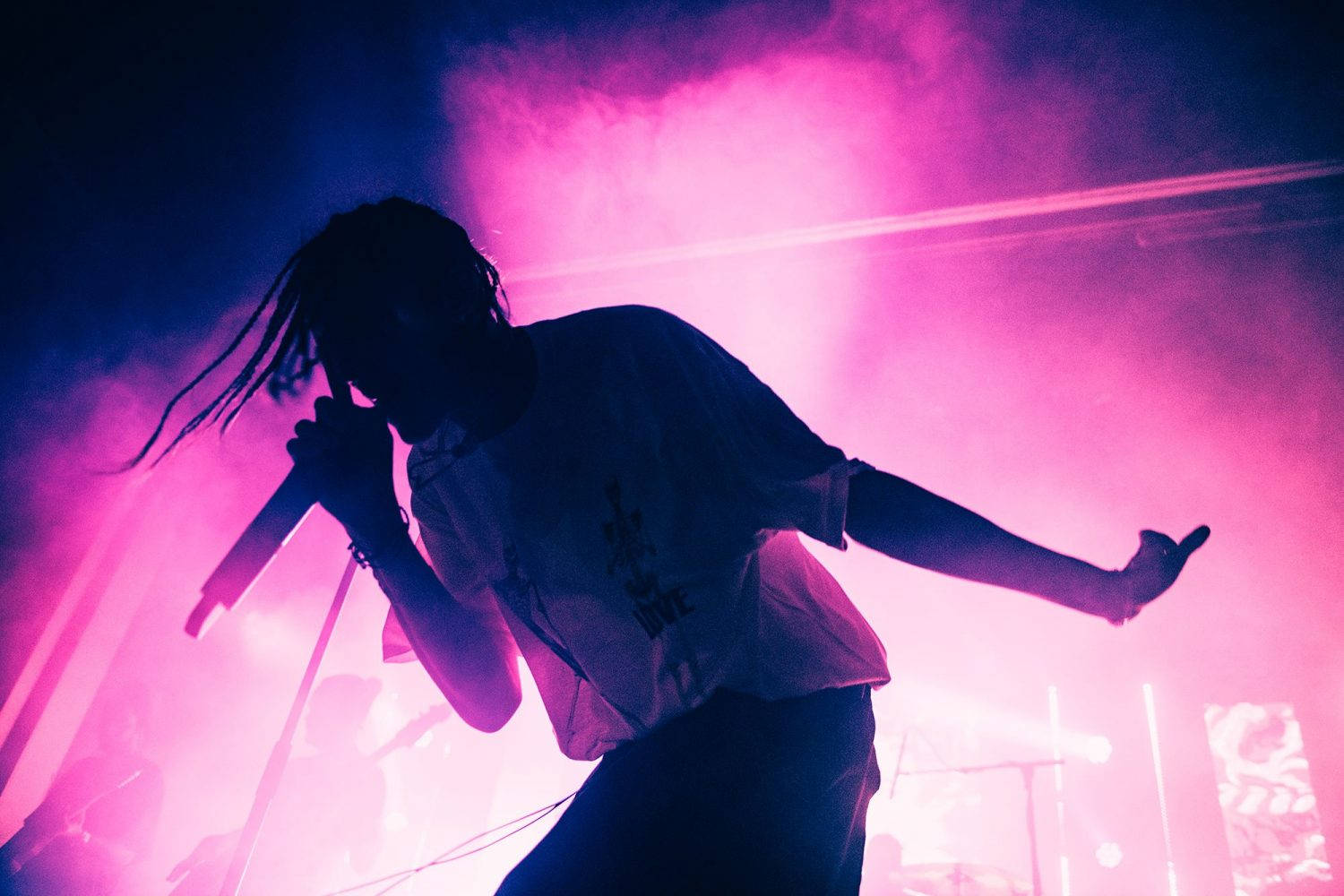 Chase Atlantic 桌布 壁紙 — 一個帶有辮子的剪影表演者在充滿活力的粉紅色和藍色舞台燈光下，煙霧繚繞中對著麥克風唱歌。