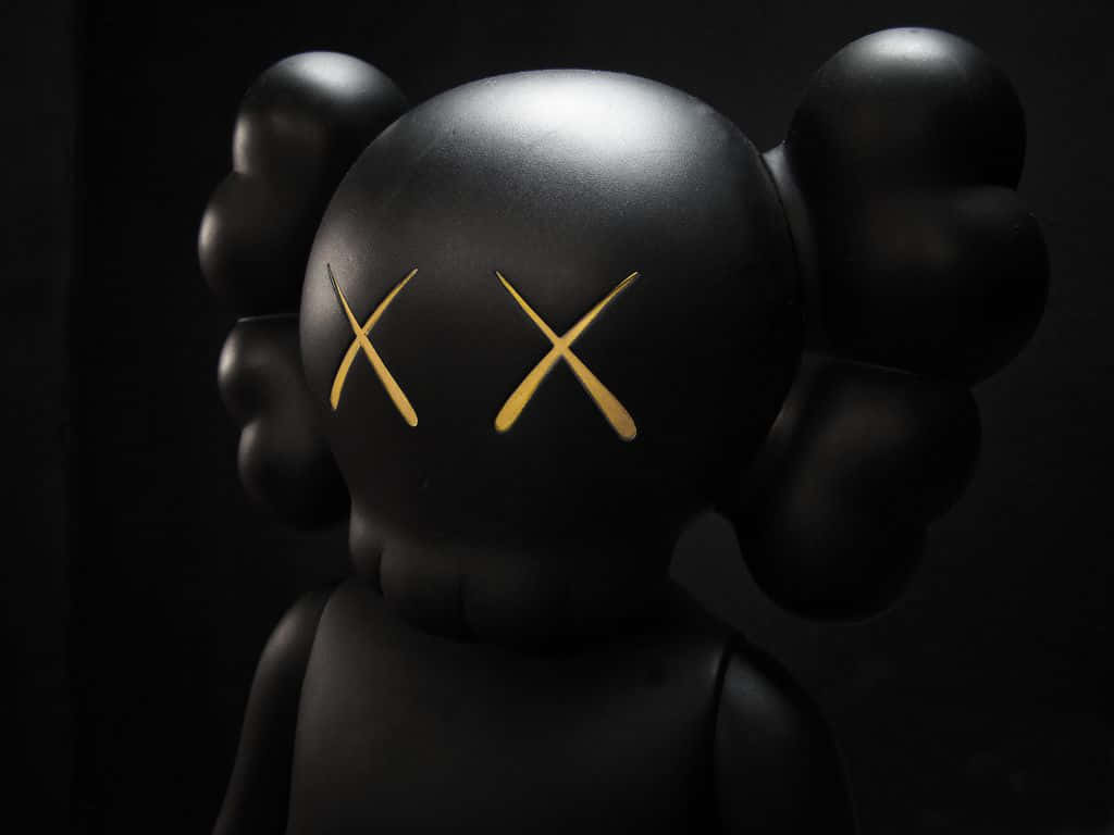 kaws pc 桌布 壁紙 — 一個帶有金色X眼睛的光澤黑色KAWS公仔，在深色背景下形成鮮明對比。