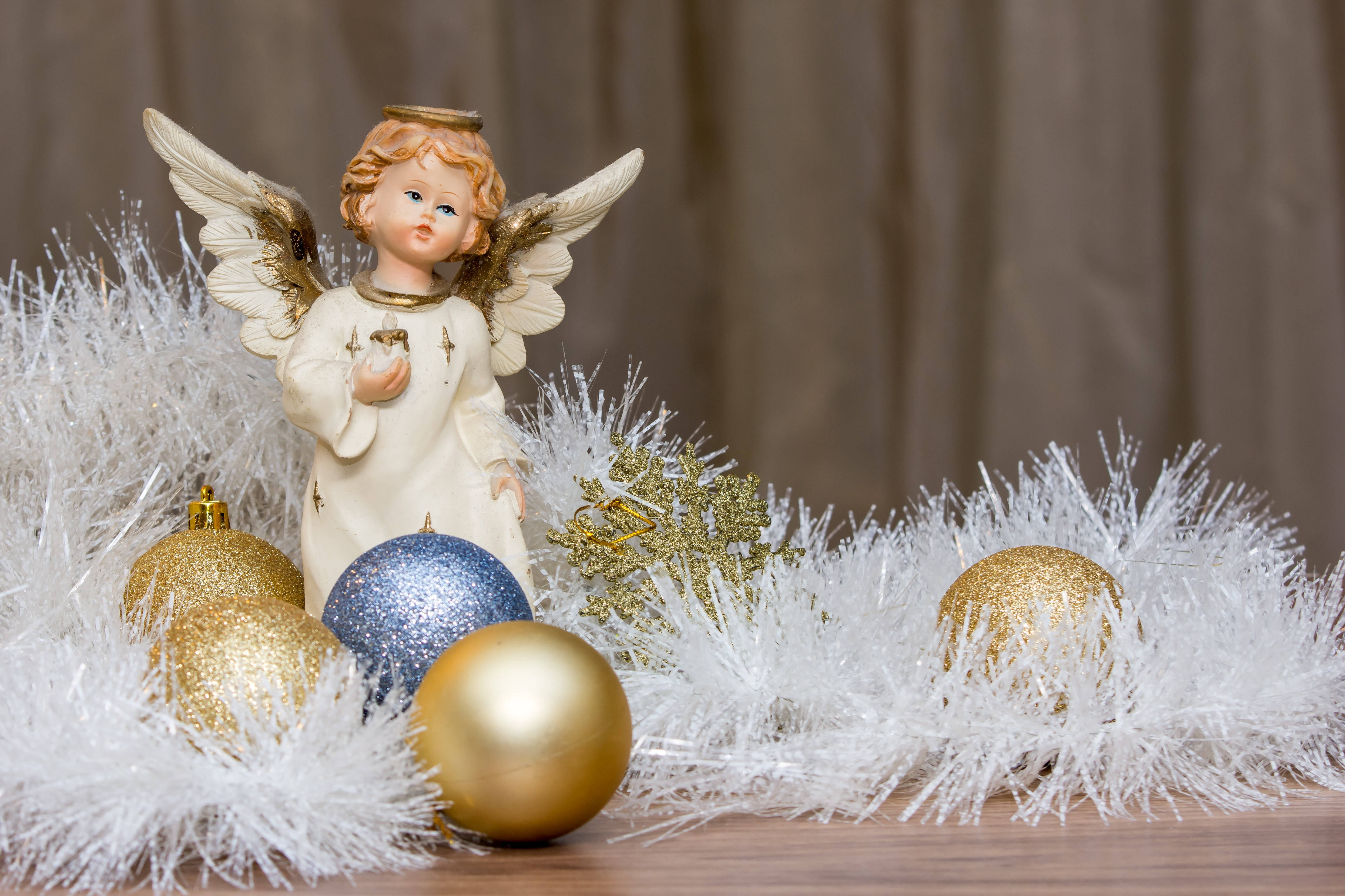 angels 桌布 壁紙 — 一個帶有金色翅膀的陶瓷天使雕像，站立在閃爍的金色和藍色裝飾品中，這些裝飾品鑲嵌在白色閃粉中。
