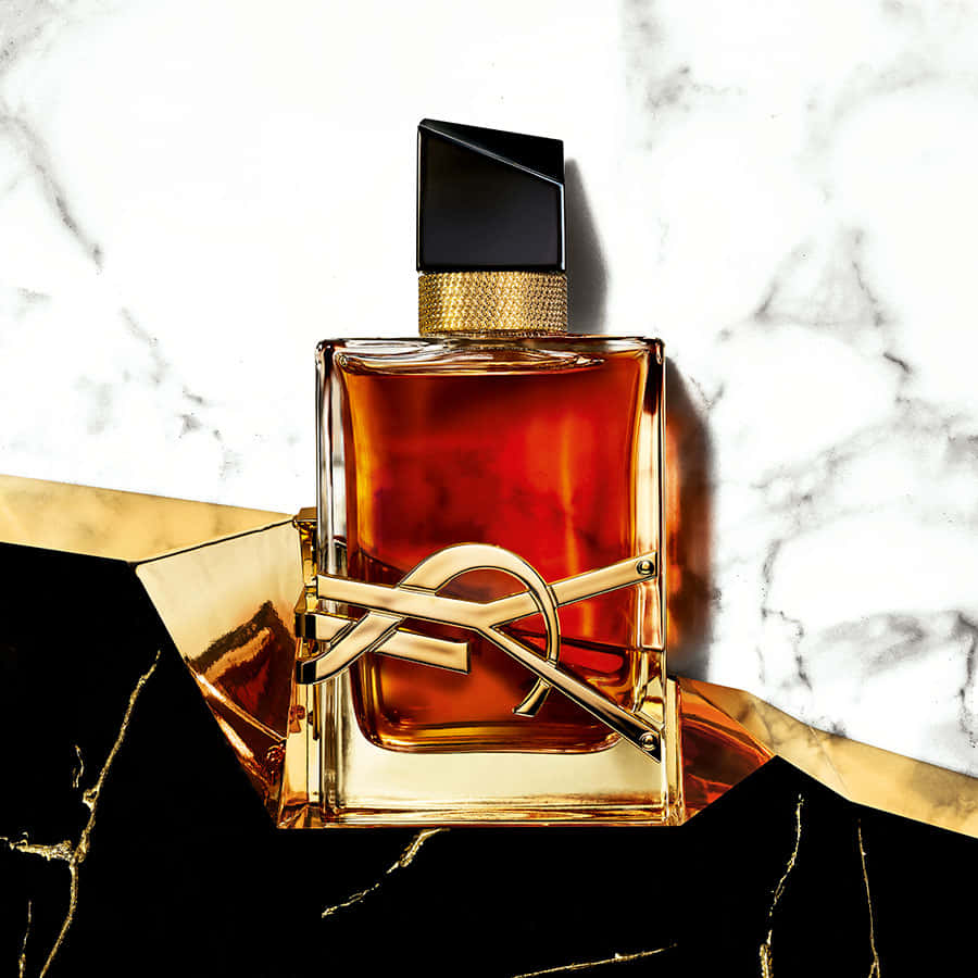 YSL 桌布 壁紙 — 一個帶有金色裝飾和黑色瓶蓋的奢華琥珀色香水瓶，放置在黑色大理石表面上，背景是白色大理石。