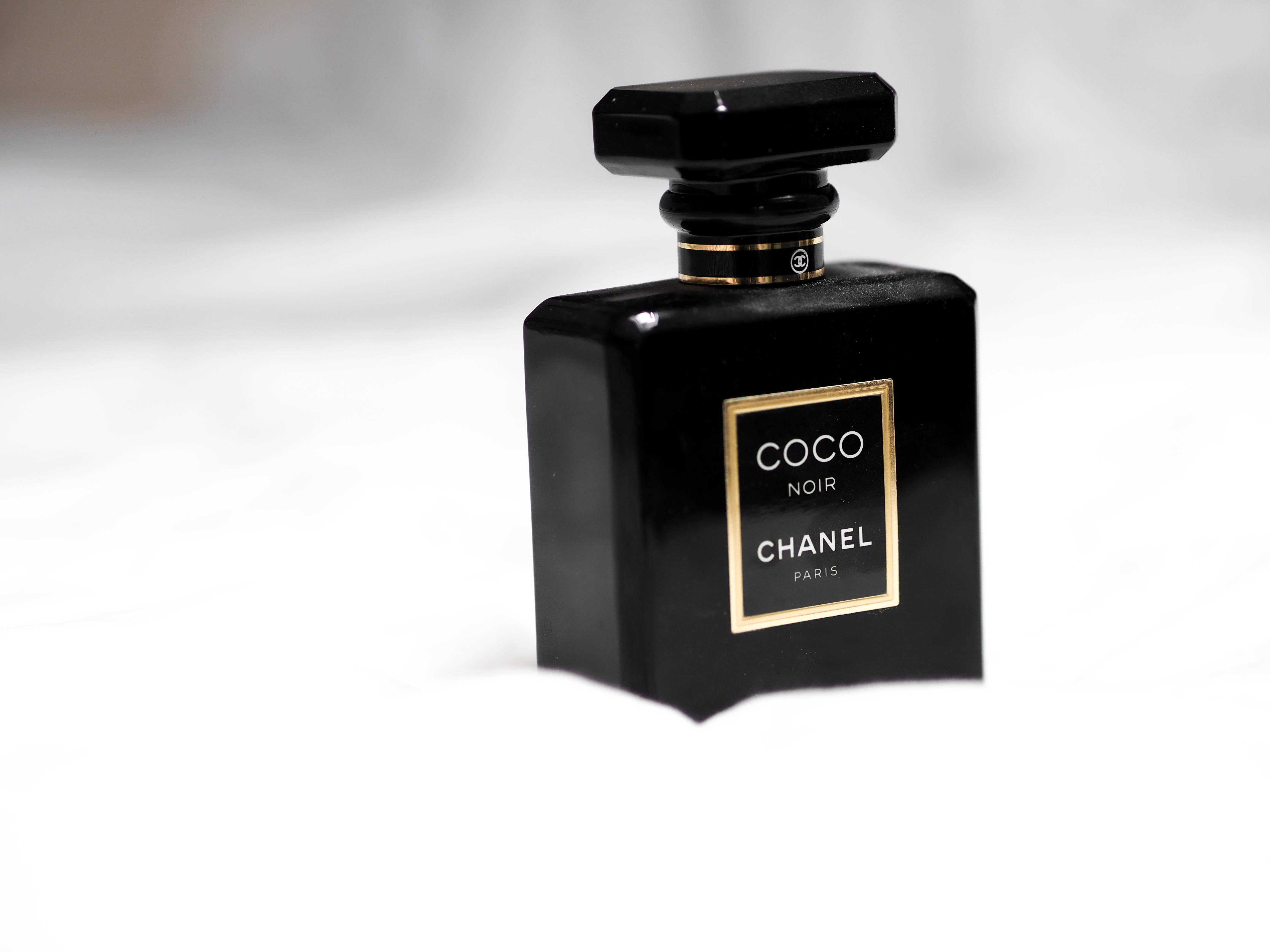 黑色美學 桌布 壁紙 — 一個帶有金色飾邊的時尚黑色 Chanel Coco Noir 香水瓶，置於明亮的白色表面上。