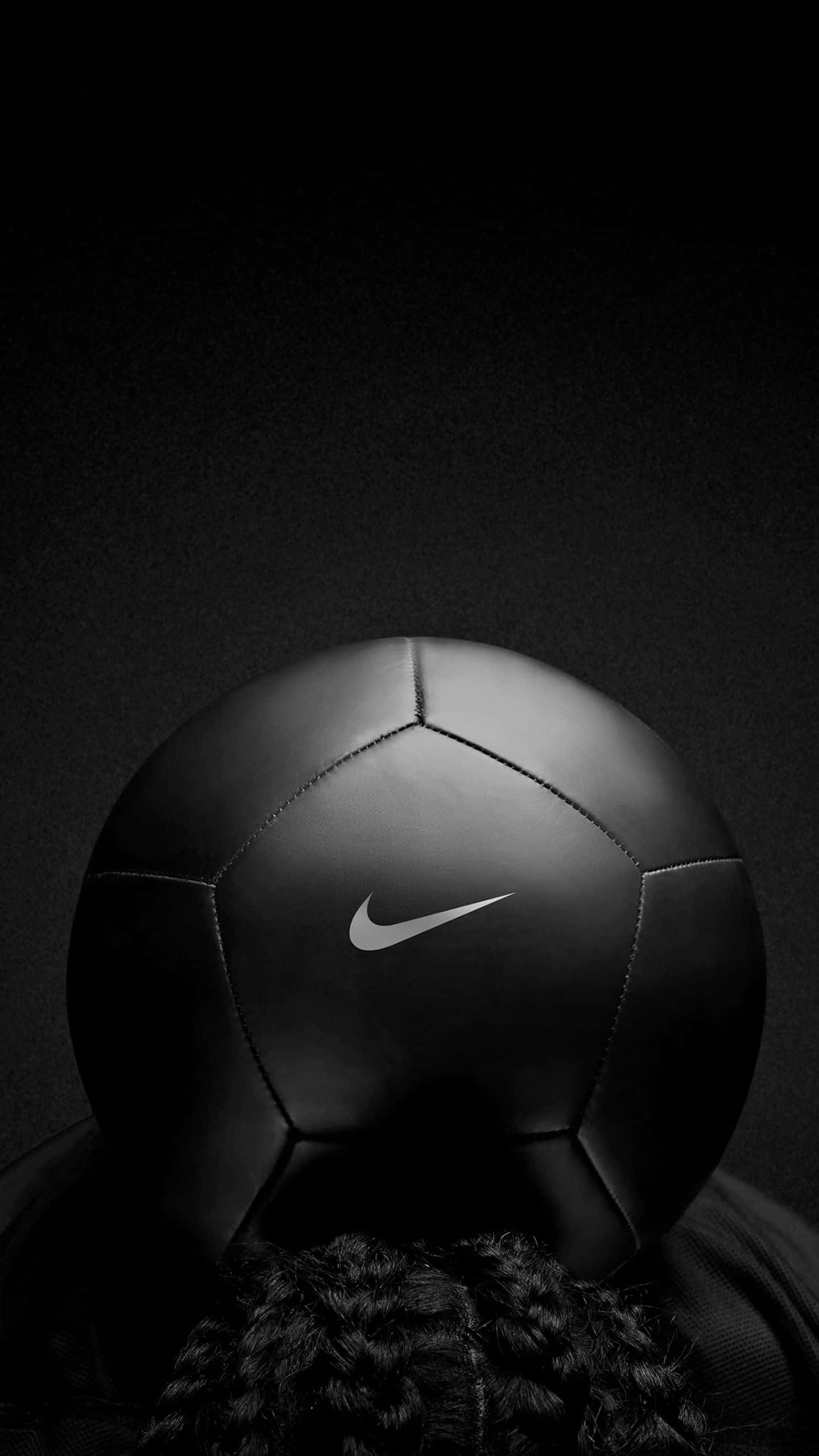 足球 桌布 壁紙 — 一個帶有銀色 swoosh 的黑色 Nike 足球放在一個人的辮子上，背景是深色漸變。