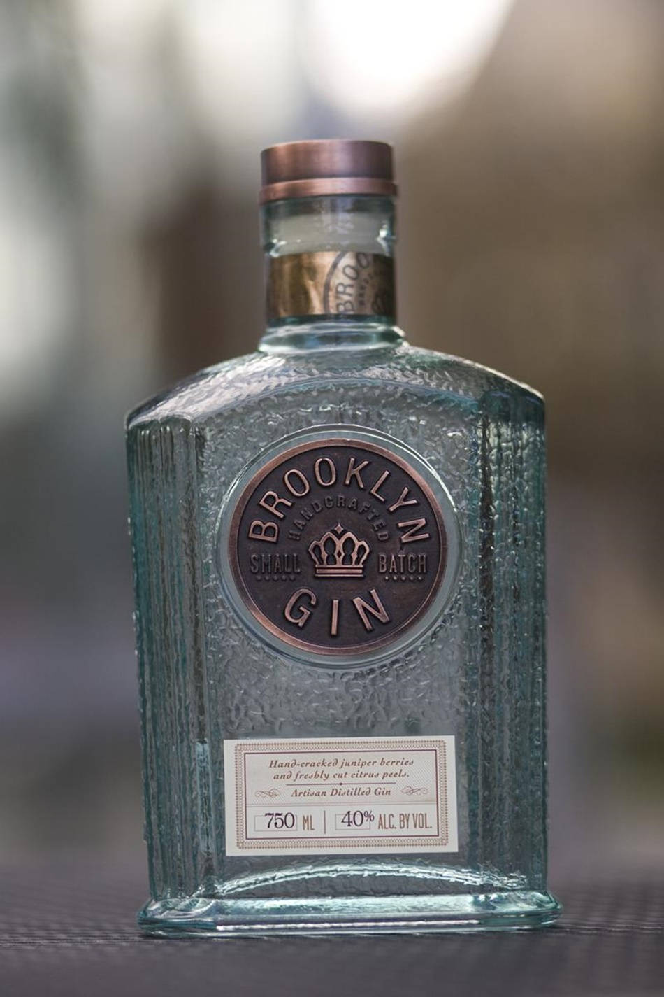 alcohol 桌布 壁紙 — 一個帶有銅蓋和標籤的布魯克林小批量琴酒紋理玻璃瓶，放在深色表面上，背景模糊。