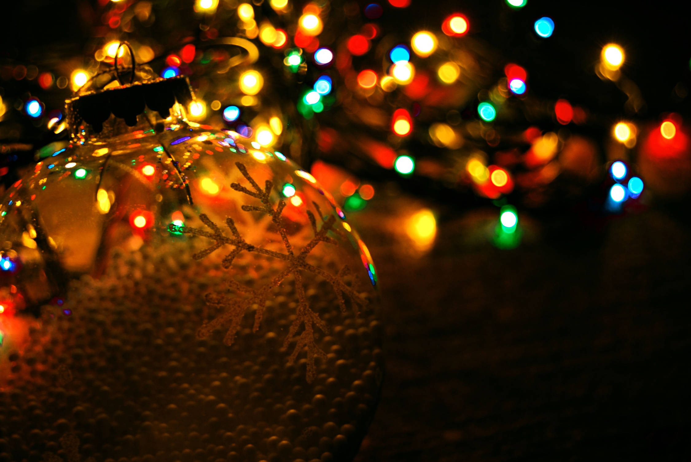 Christmas Balls 桌布 壁紙 — 一個帶有雪花圖案的紋理玻璃聖誕裝飾的特寫，在色彩繽紛的散景燈光背景下溫暖地發光。