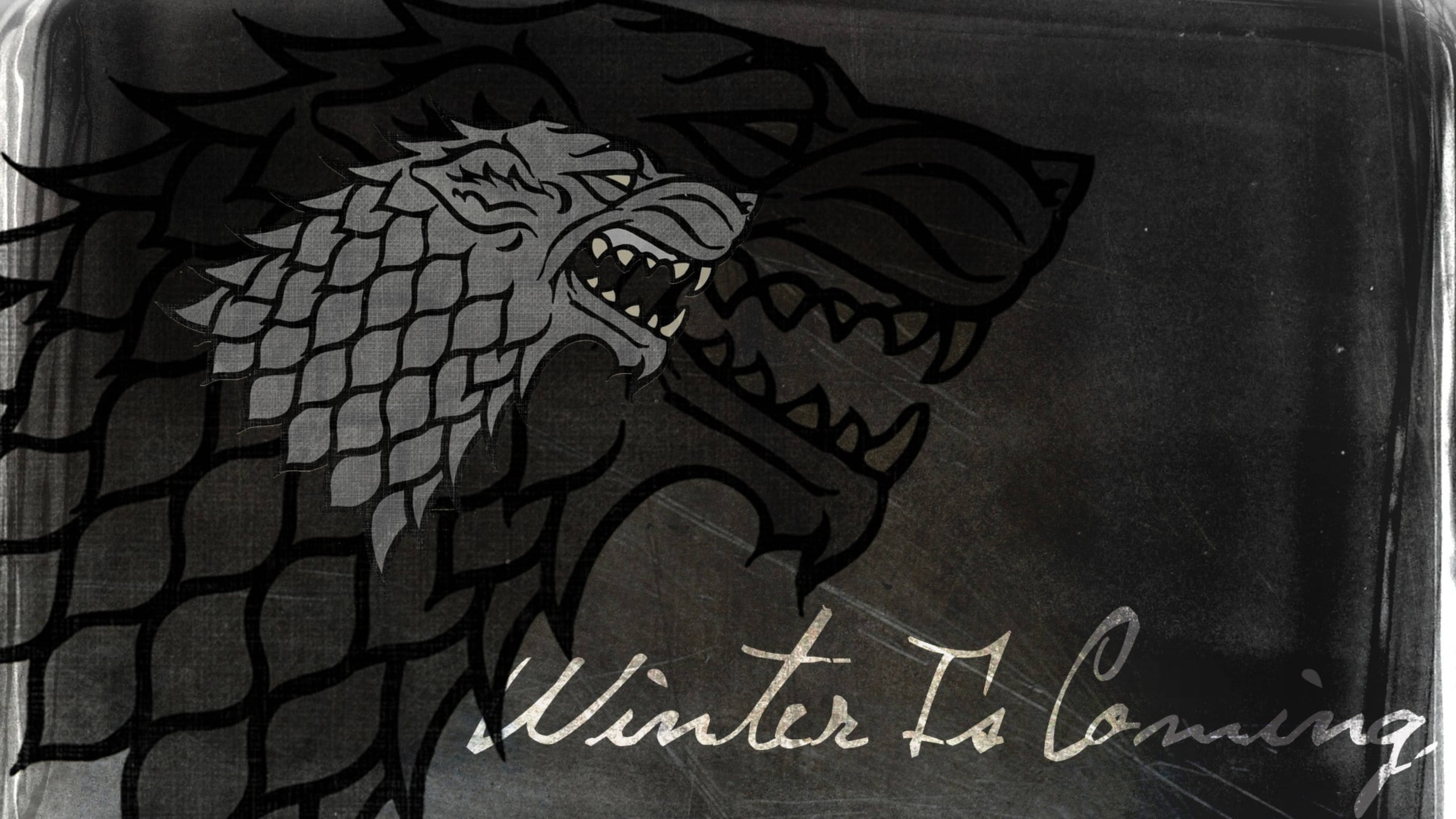 House Stark 桌布 壁紙 — 一個帶有露齒和鱗片的灰色冰原狼頭，具有威脅性，置於有刮痕的深色背景上，並有草書字體的Winter Is Coming字句。