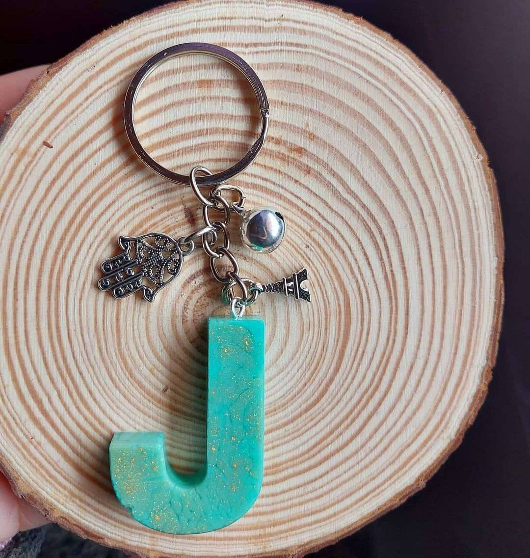 J 桌布 壁紙 — 一個帶有飾品的青綠色閃粉字母J鑰匙圈，放在由手托著的木切片上。