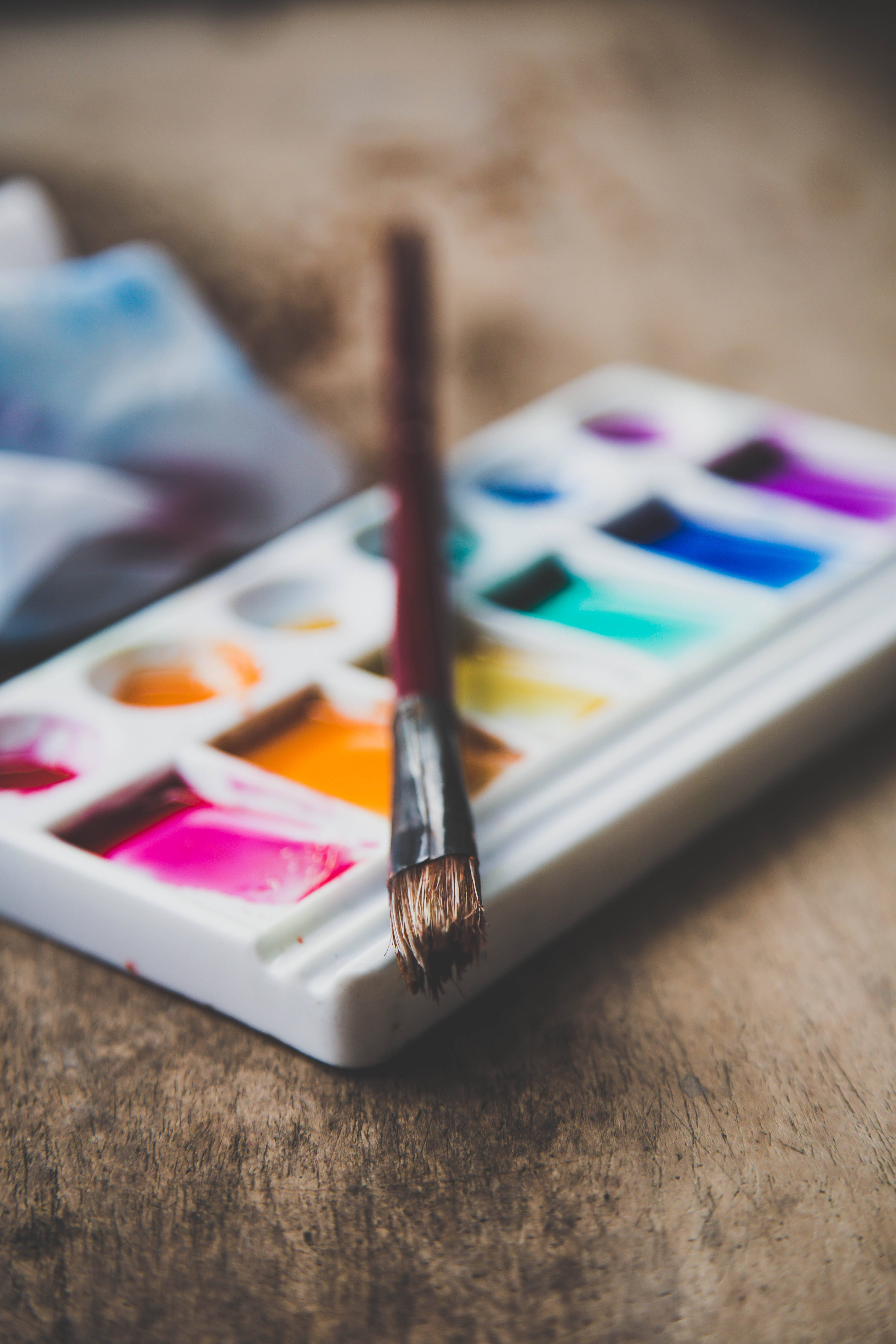 Watercolor 桌布 壁紙 — 一個帶有鮮豔色調的水彩顏料調色板和一支畫筆放在質樸的木質表面上。