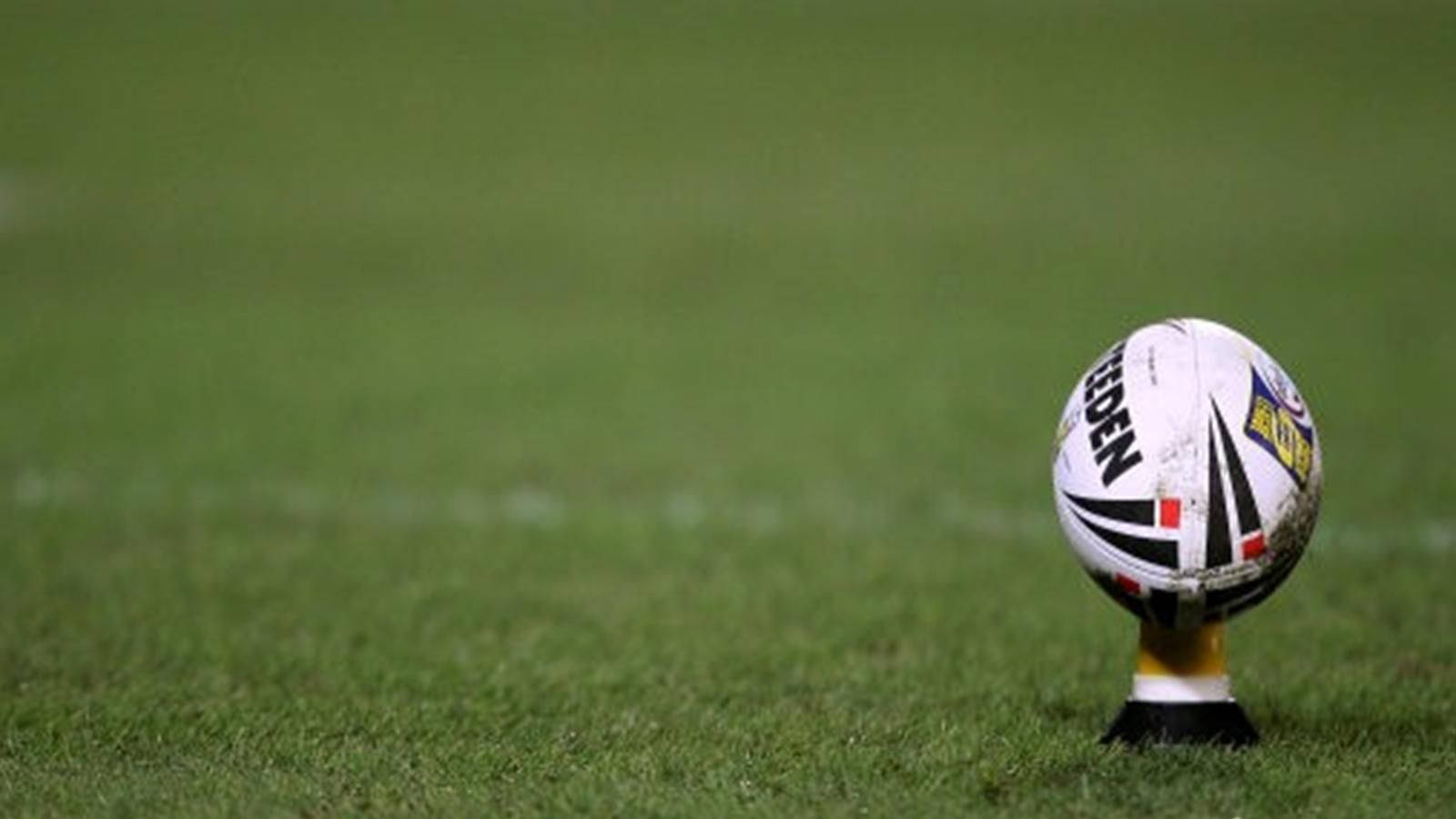 Nrl 桌布 壁紙 — 一個帶有黑色和黃色標記的白色橄欖球直立於一個充滿活力的綠色草地場地上的球座上。