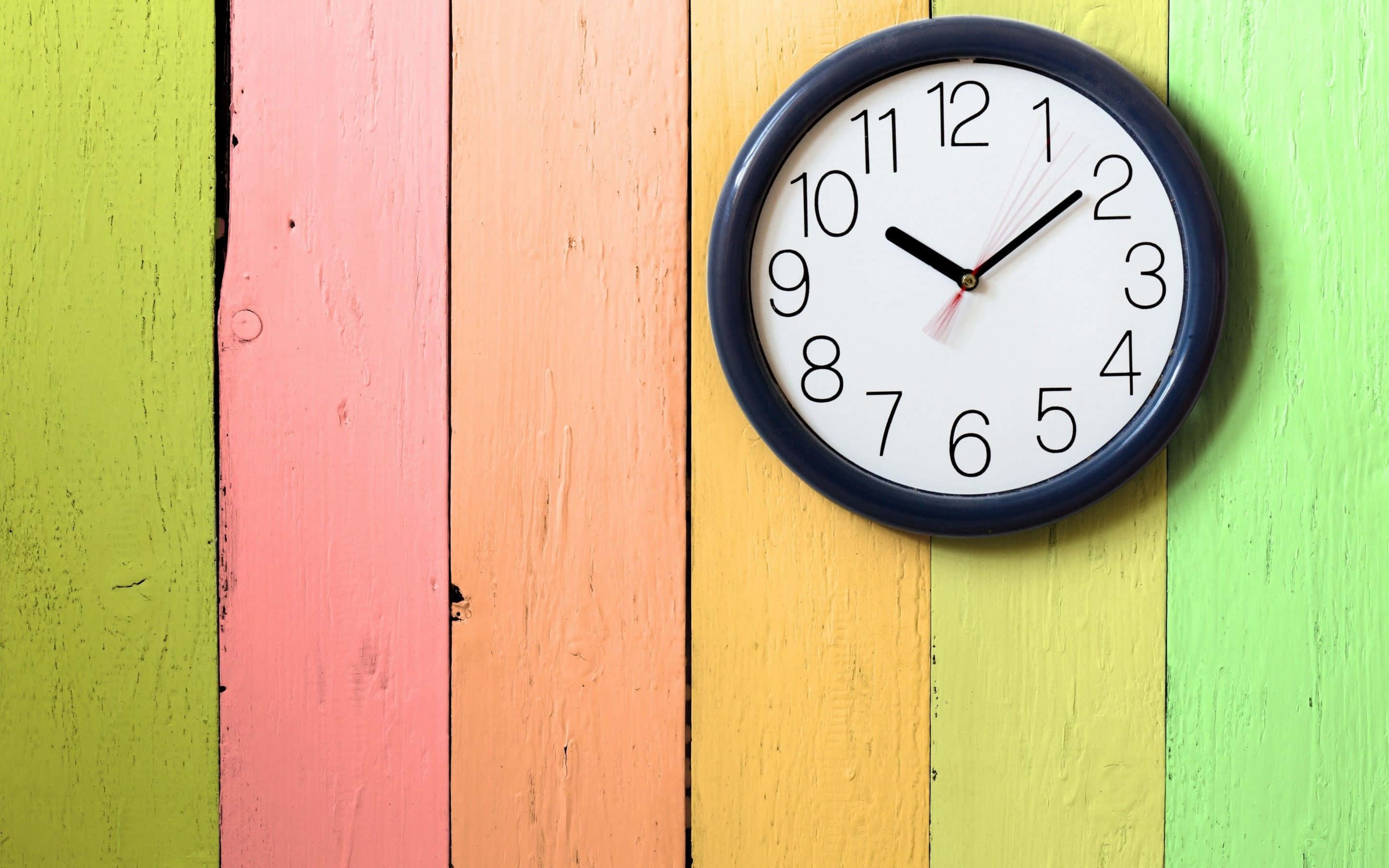Clock 桌布 壁紙 — 一個帶有黑色指針的圓形指針時鐘掛在由彩虹色調鮮豔油漆木板組成的牆上。