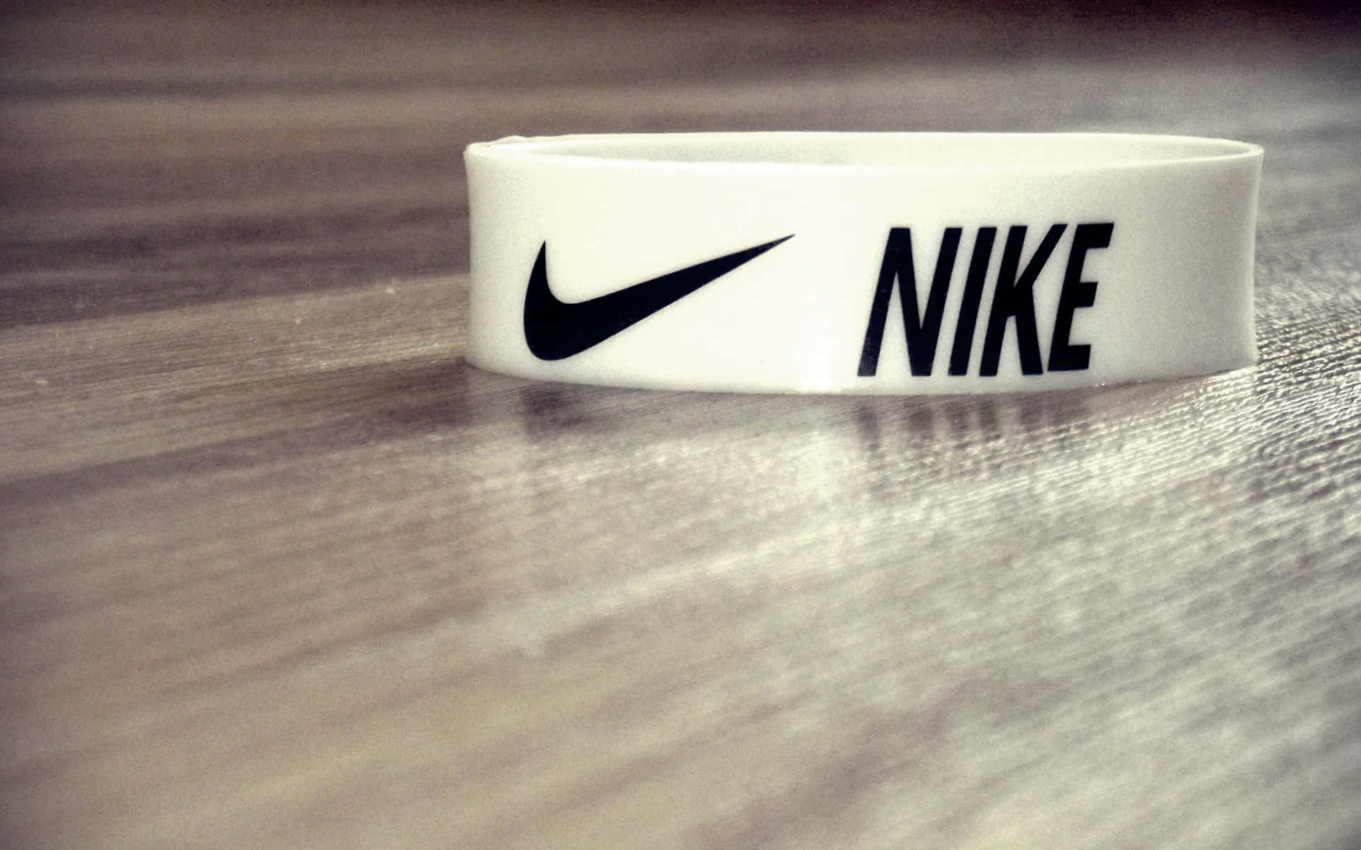 Nike 桌布 壁紙 — 一個帶有黑色標誌的白色Nike腕帶，放置在紋理木質表面上，焦點柔和。