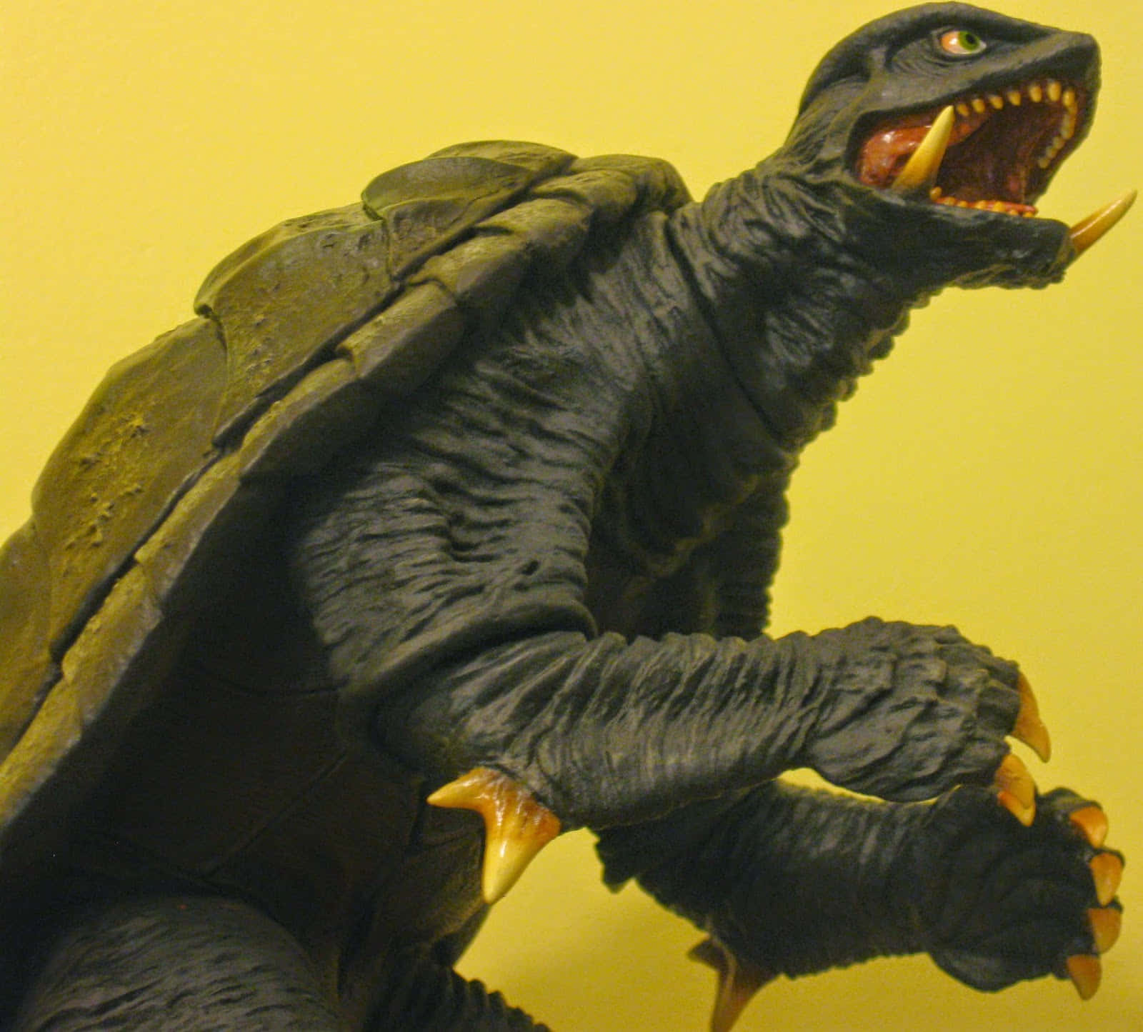 Gamera 桌布 壁紙 — 一個帶有龜殼的威脅性黑色哥斯拉式怪物在純黃色背景上猛烈咆哮。