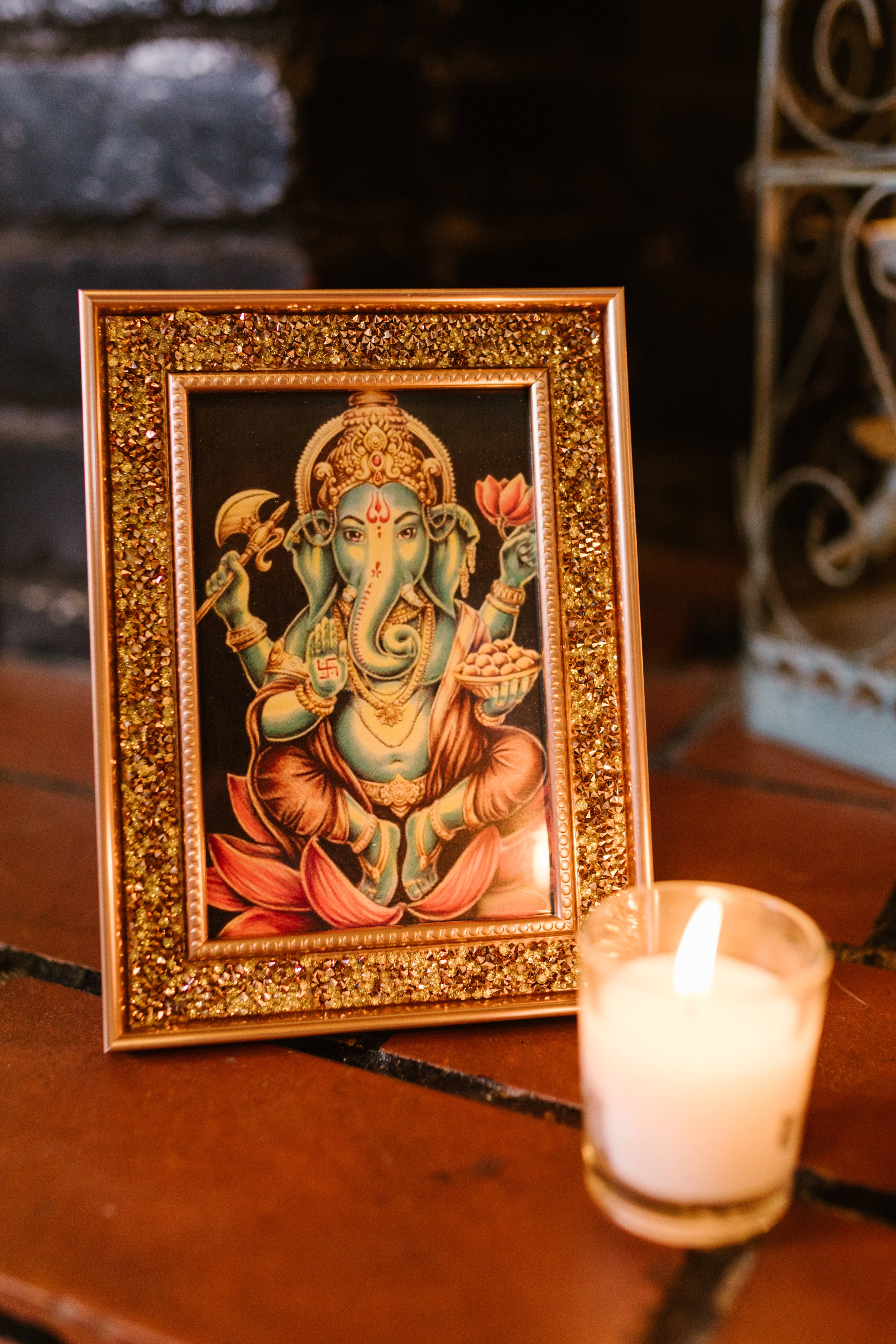 ganesh 4K 桌布 壁紙 — 一個帶框的象神畫像，旁邊有一根點燃的蠟燭放在木質表面上。