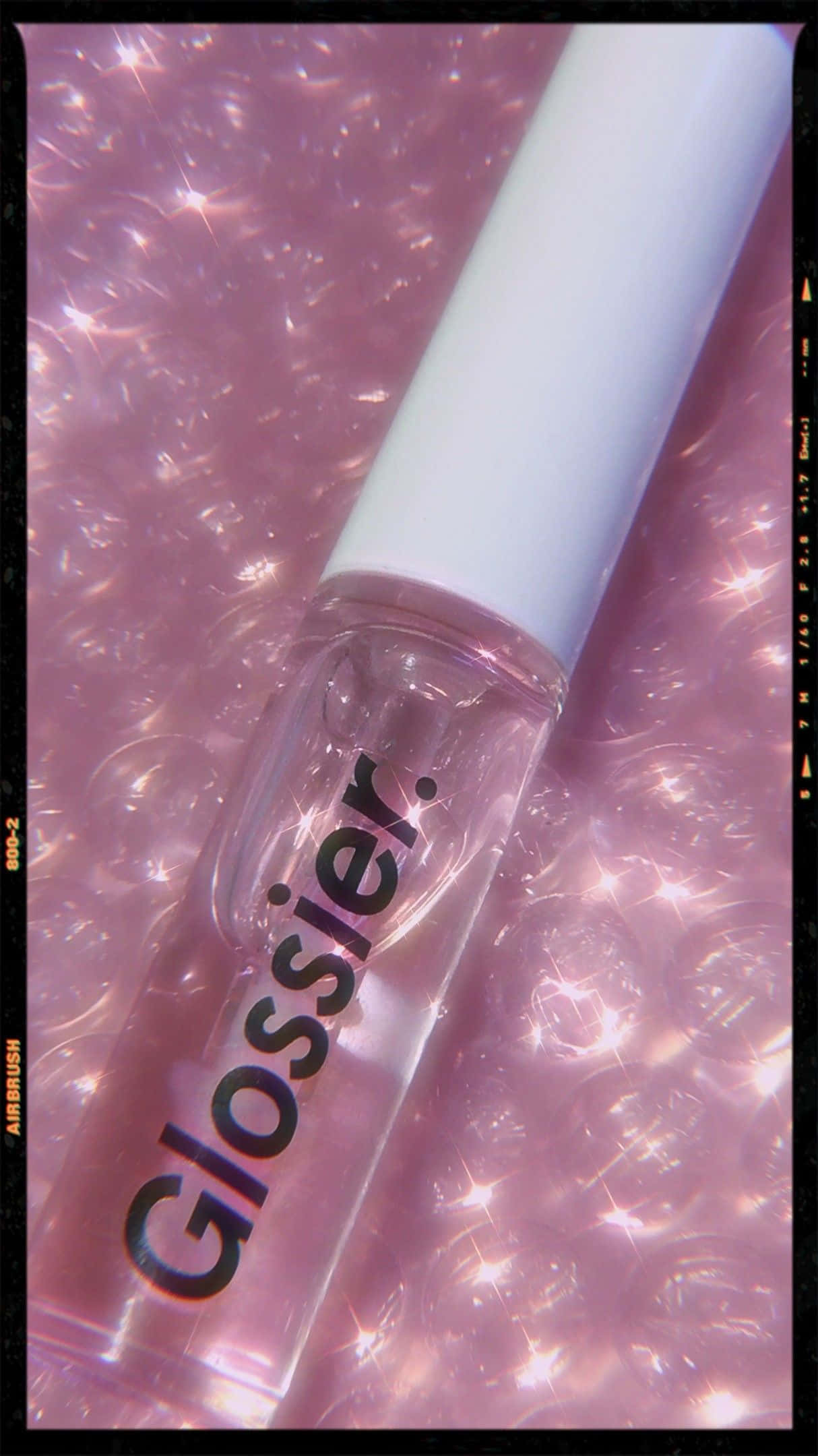Cosmetic 桌布 壁紙 — 一個帶白色蓋子的透明 Glossier 唇彩瓶放在閃爍的粉紅色泡泡背景上，帶有底片顆粒感。