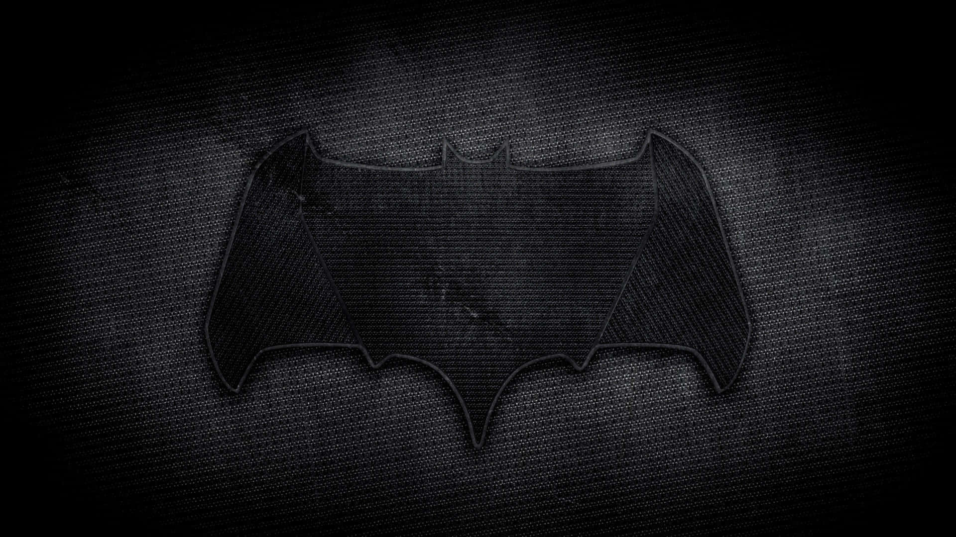 bat 桌布 壁紙 — 一個帶紋理的黑色蝙蝠標誌在深色布料背景上隱隱發光，帶有粗獷的電影感。