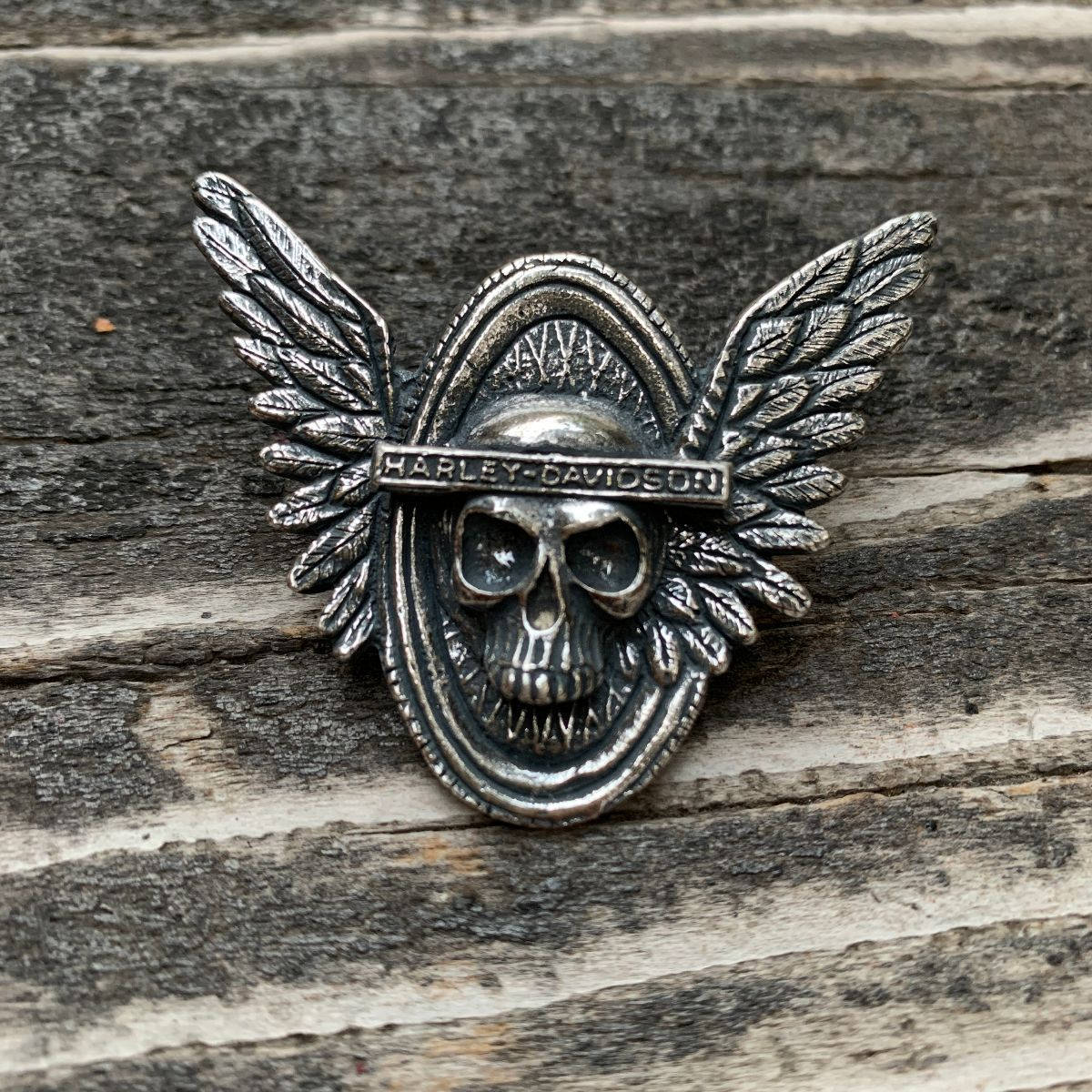 Harley 桌布 壁紙 — 一個帶翅膀的金屬哈雷戴維森骷髏別針放在風化的灰色木頭上。