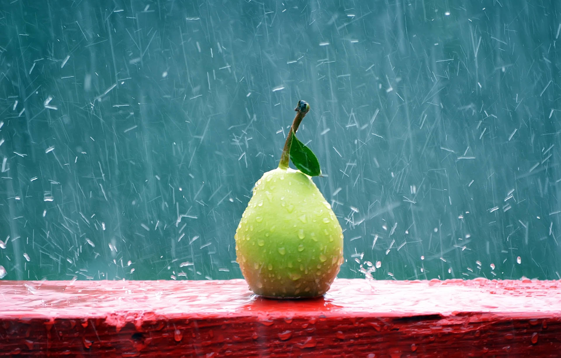 一個帶葉的綠色梨子放在紅色表面上，周圍有雨落下。 — 圖片 GIF 壁紙