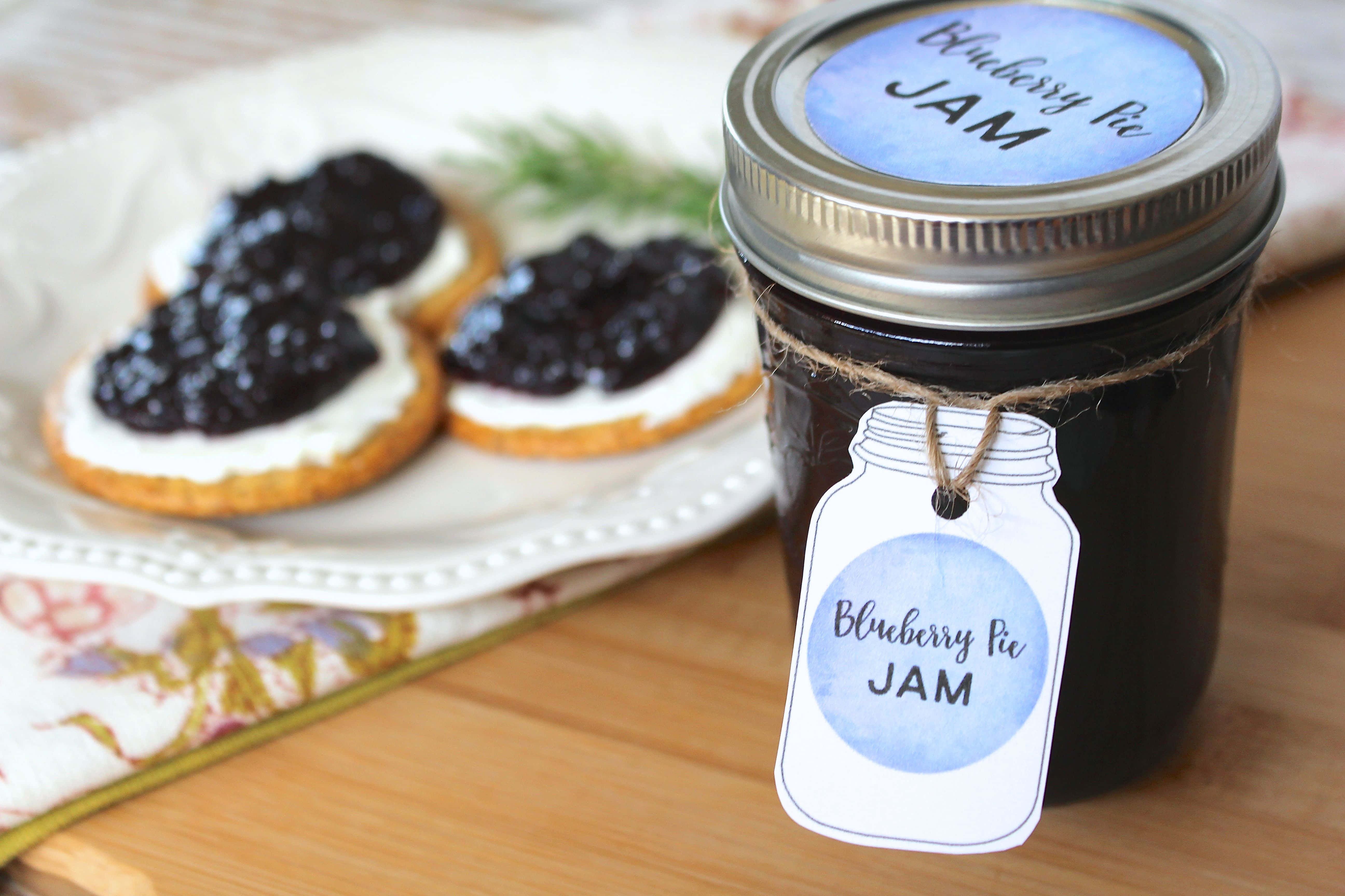 Blueberry Jam 桌布 壁紙 — 一個帶麻繩標籤的藍莓派果醬罐，旁邊放著塗上果醬的餅乾，在木桌上。