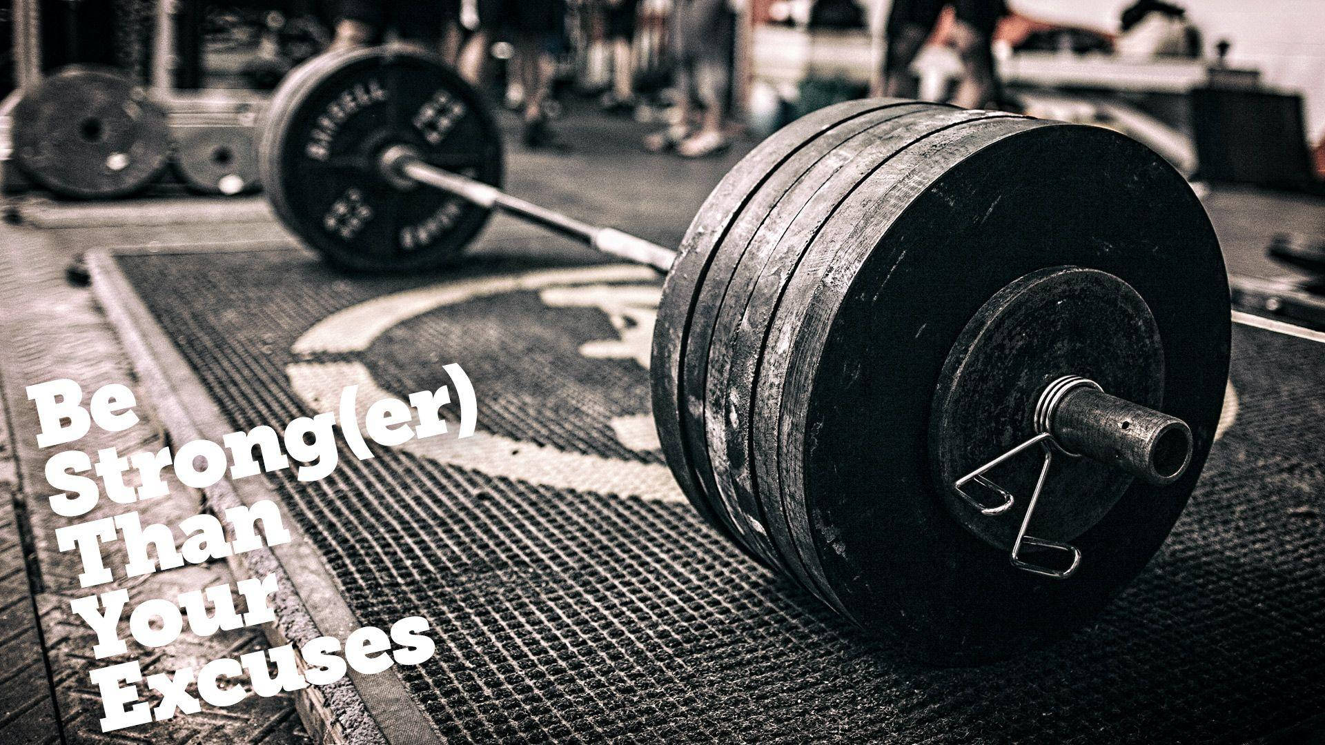 Barbell 桌布 壁紙 — 一個帶黑色槓片的沉重槓鈴放在健身房地板墊上，上面有勵志文字疊加。