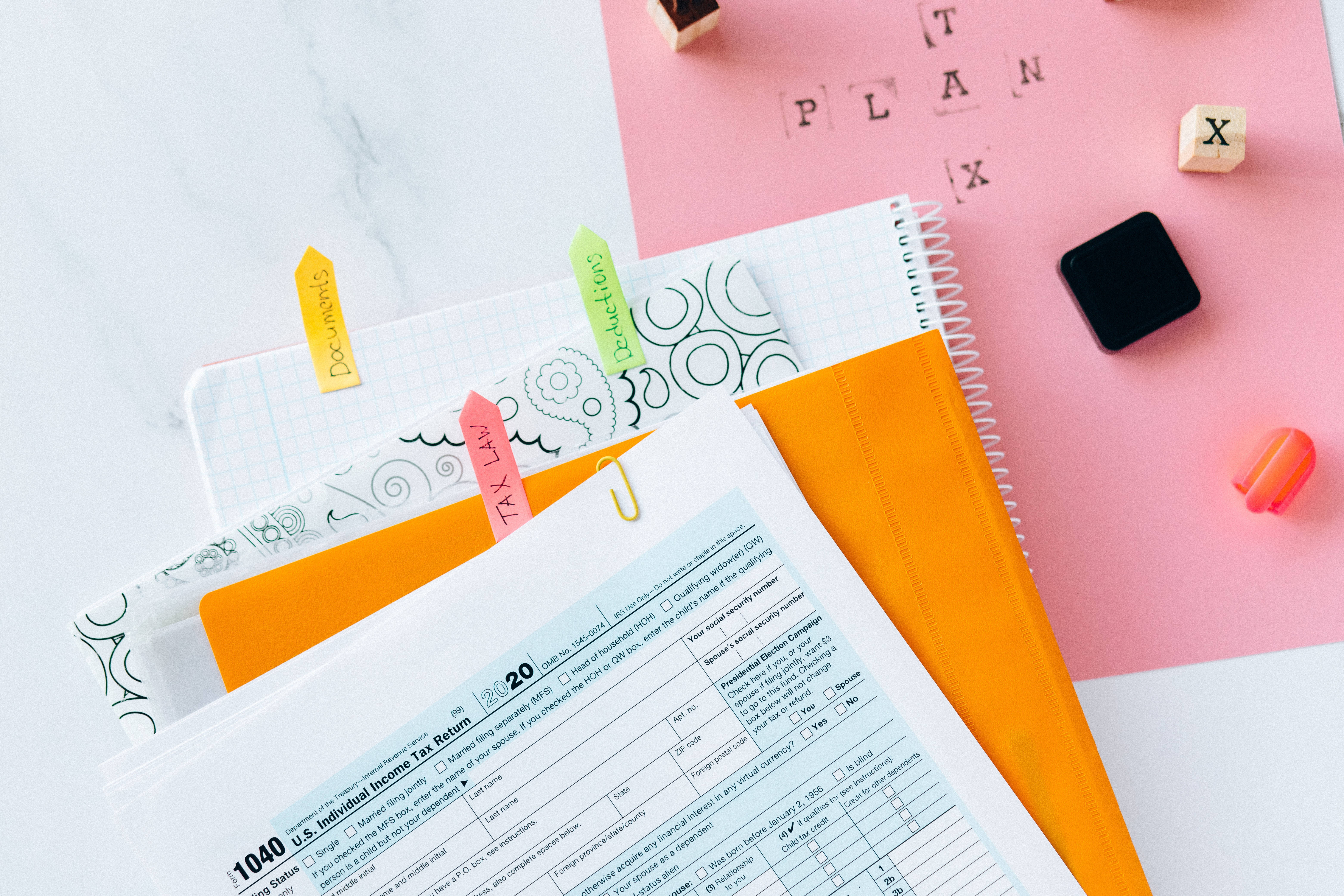 Chartered Accountant 桌布 壁紙 — 一個平鋪擺放的1040稅表，配有彩色文件夾和拼出plan字母積木，放在大理石和粉紅色表面上。