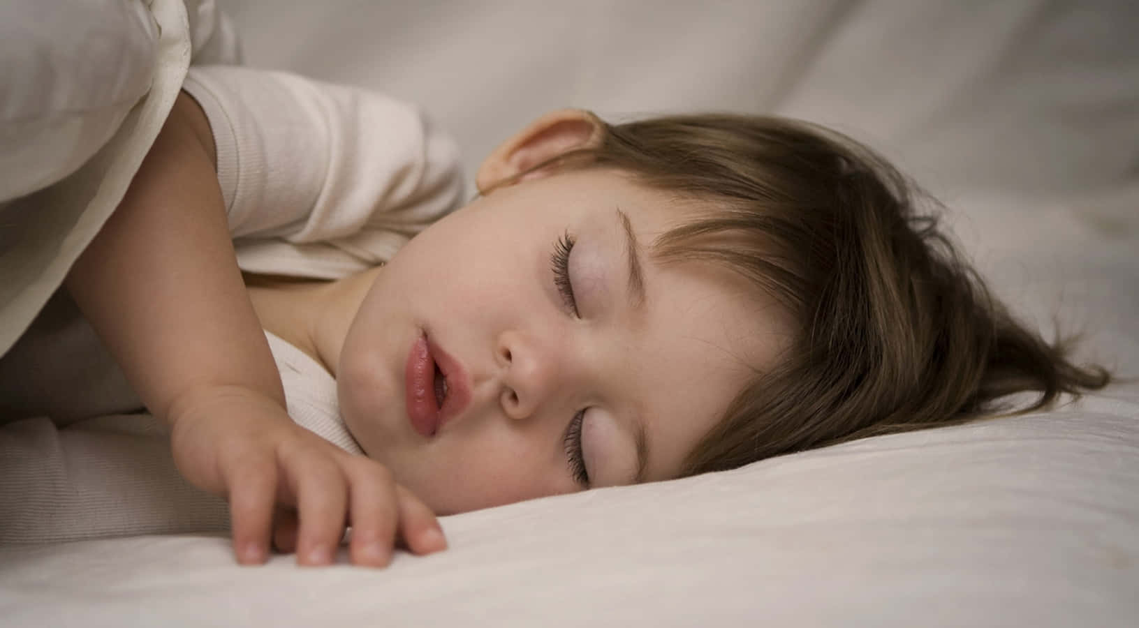 Sleep 桌布 壁紙 — 一個平靜的幼兒在柔軟的白色枕頭上閉上眼睛，手輕輕放在臉頰旁邊，睡得香甜。