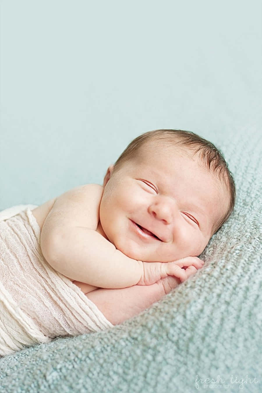 Infant 桌布 壁紙 — 一個平靜的新生嬰兒包裹在奶油色布料中，在柔軟的藍綠色紋理毯子上幸福地微笑。