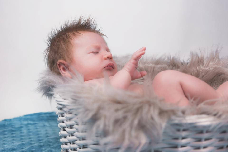 Very Cute Baby 桌布 壁紙 — 一個平靜的新生嬰兒在一個襯有柔軟灰色毛皮的白色柳條籃子裡，對著純白色背景安穩地睡著。