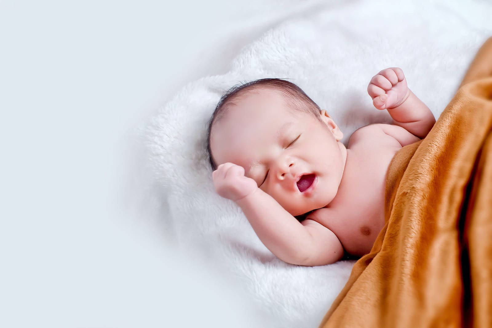 Baby Boy 桌布 壁紙 — 一個平靜的新生嬰兒在柔軟的白色毛毯上安睡，部分被溫暖的金棕色毛毯覆蓋，嘴巴微微張開。