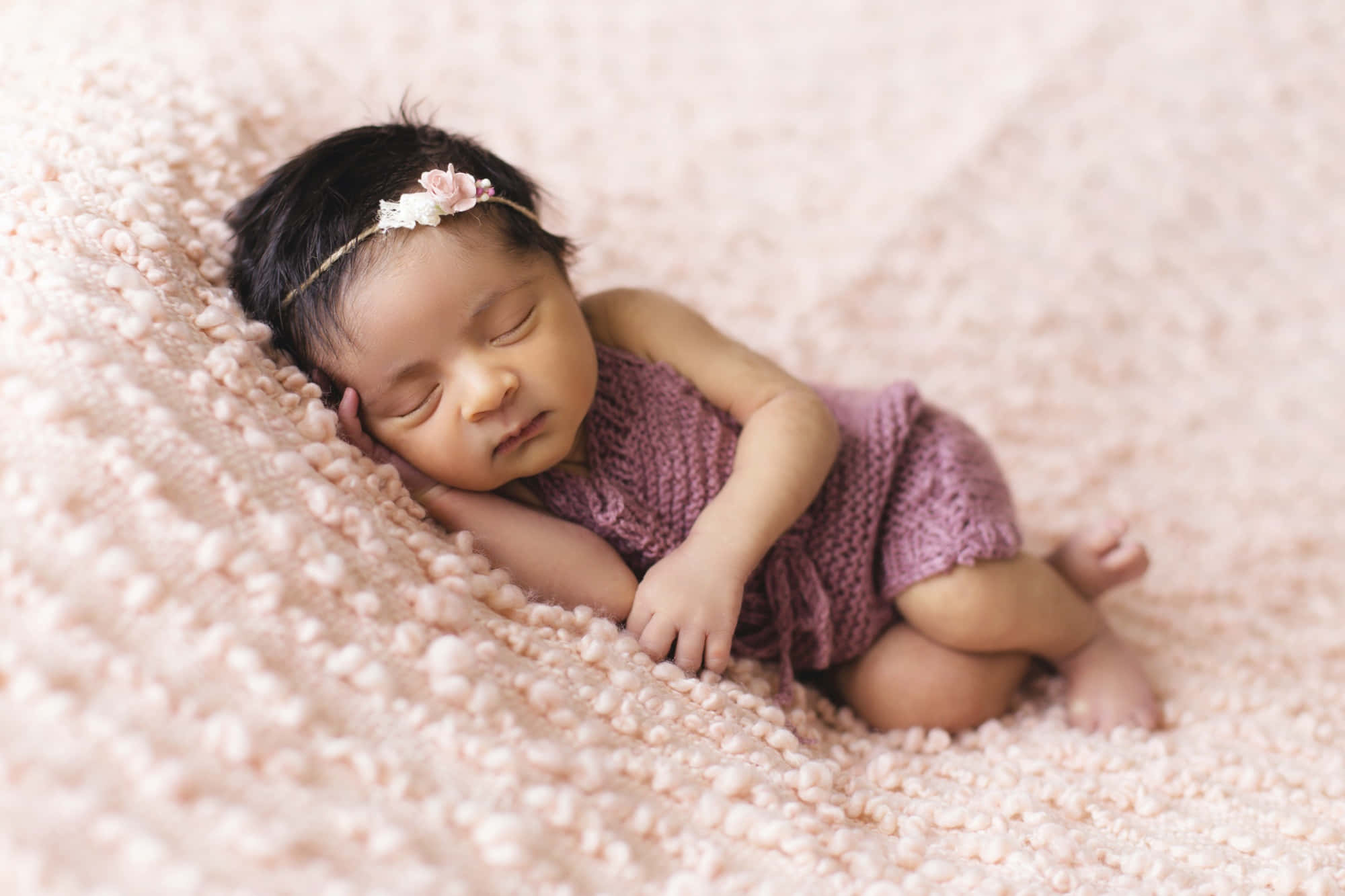 Infant 桌布 壁紙 — 一個平靜的新生嬰兒在柔軟的粉紅色紋理毛毯上安睡，穿著相配的針織服裝和花卉頭帶。