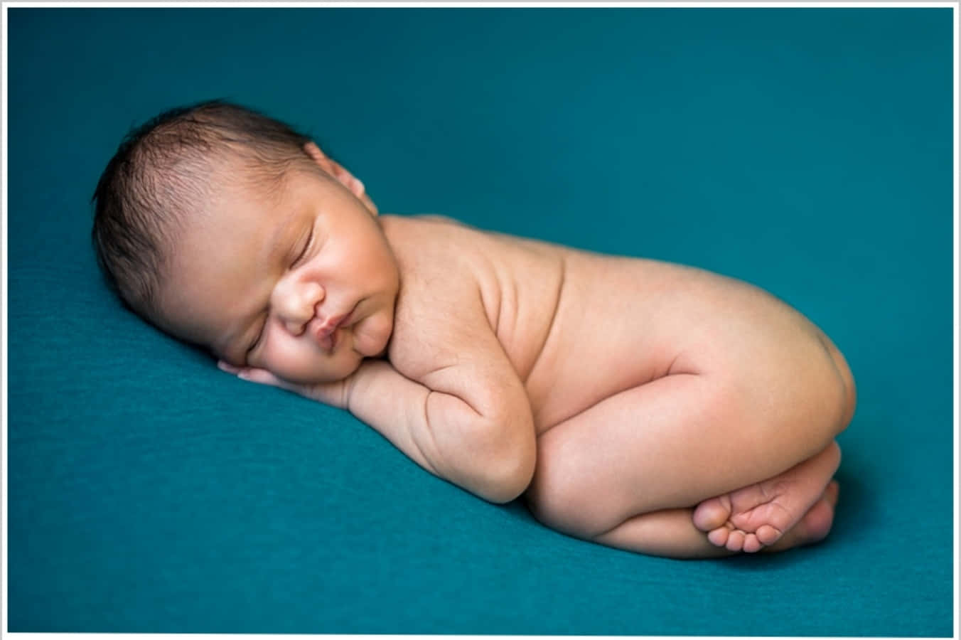 Infant 桌布 壁紙 — 一個平靜的新生嬰兒在純青色背景上蜷縮入睡，柔和光線突顯細嫩肌膚和幼細毛髮。