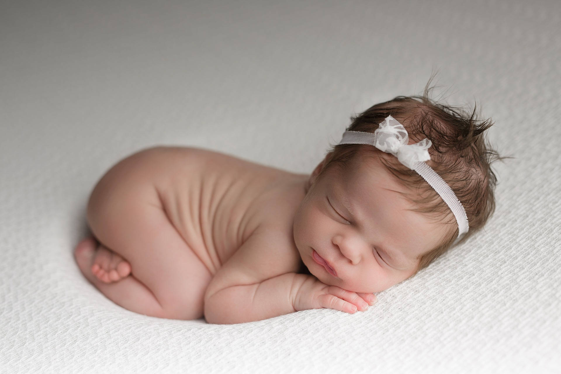 Very Cute Baby 桌布 壁紙 — 一個平靜的新生嬰兒蜷縮在柔軟的白色紋理毛毯上睡覺，戴著精緻的白色頭帶。