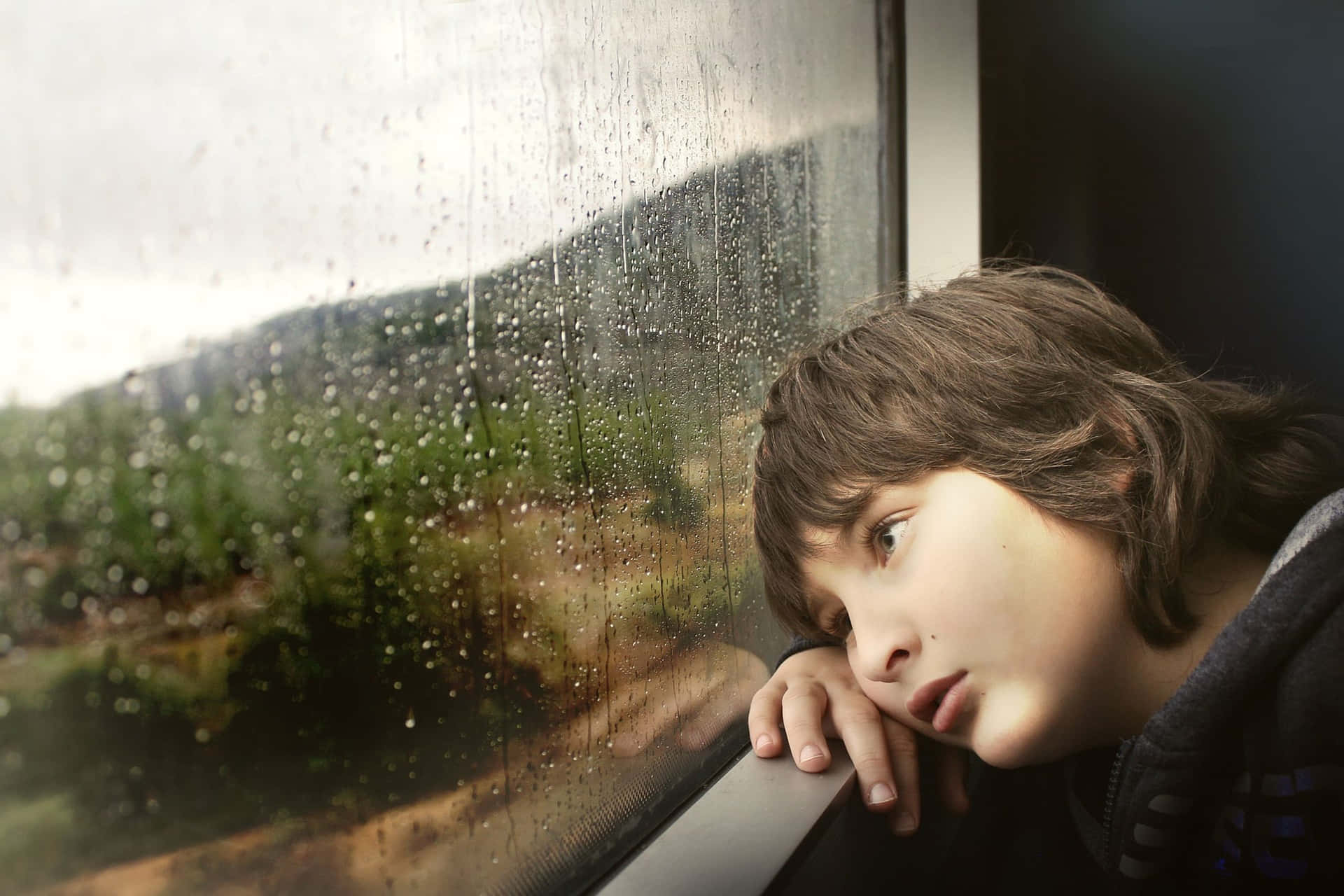 Alone 桌布 壁紙 — 一個年輕人沉思地望著火車窗外雨絲斑駁的模糊綠色風景。