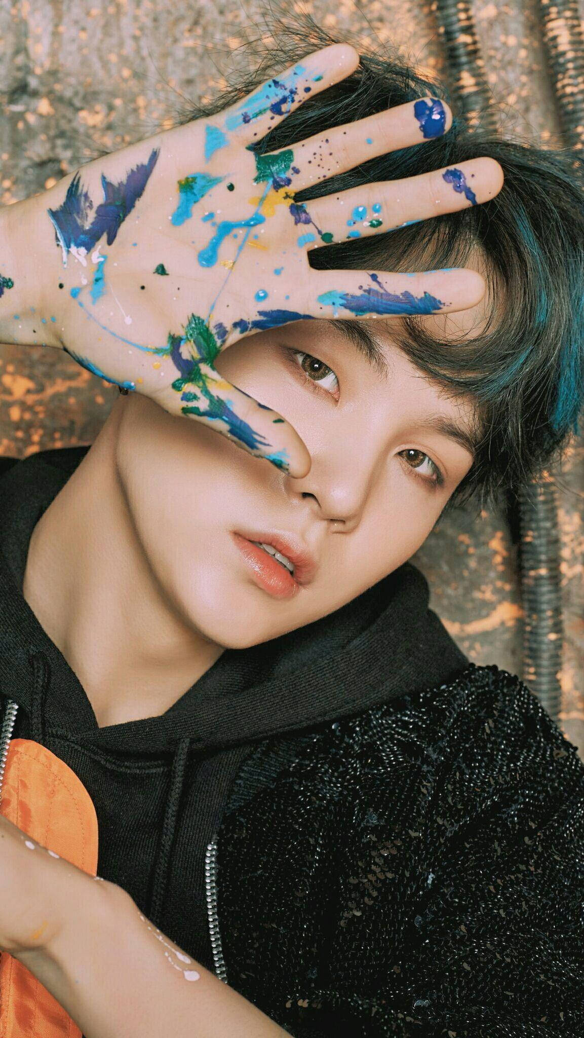 Suga Bts 桌布 壁紙 — 一個年輕人用沾滿油漆的手遮住半邊臉，背景有紋理。