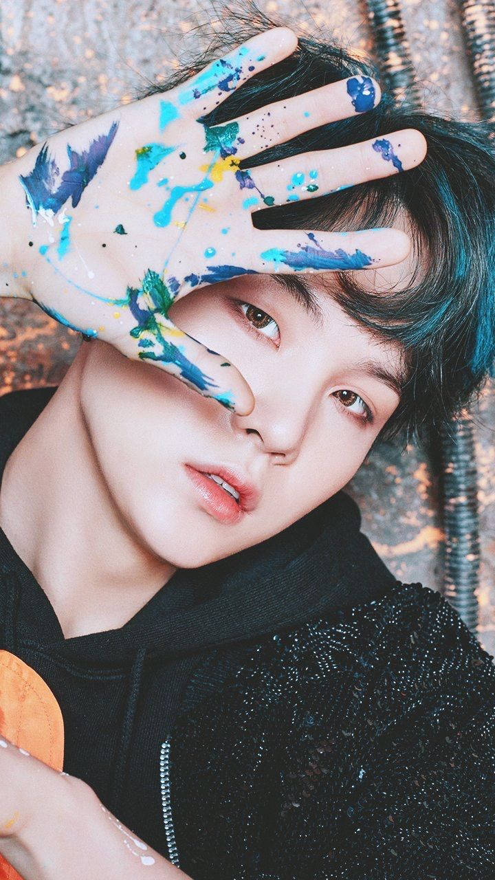 BTS 鎖定螢幕 桌布 壁紙 — 一個年輕人用沾滿油漆的手遮住半邊臉，背景有紋理。