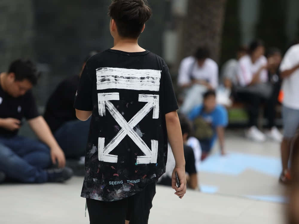 Off White 桌布 壁紙 — 一個年輕人穿著黑色Off White T恤，上面有大型白色箭頭標誌和油漆飛濺細節，走開。