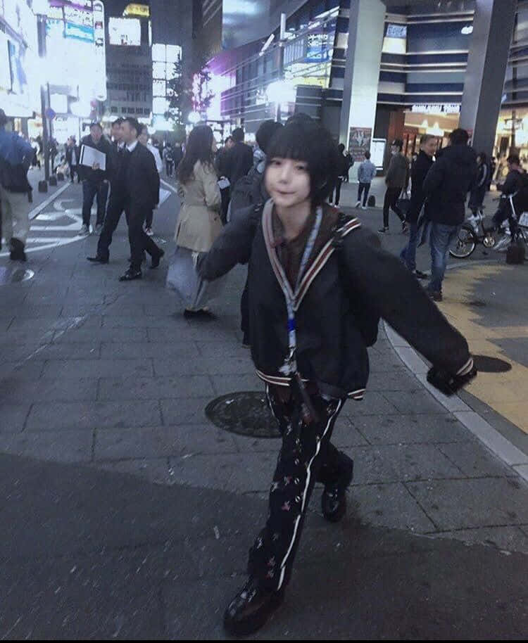 垃圾美學 桌布 壁紙 — 一個年輕人穿著黑色水手風格服裝，戴著兔耳朵，在夜晚霓虹燈閃爍的繁忙城市人行道上開心地擺姿勢。
