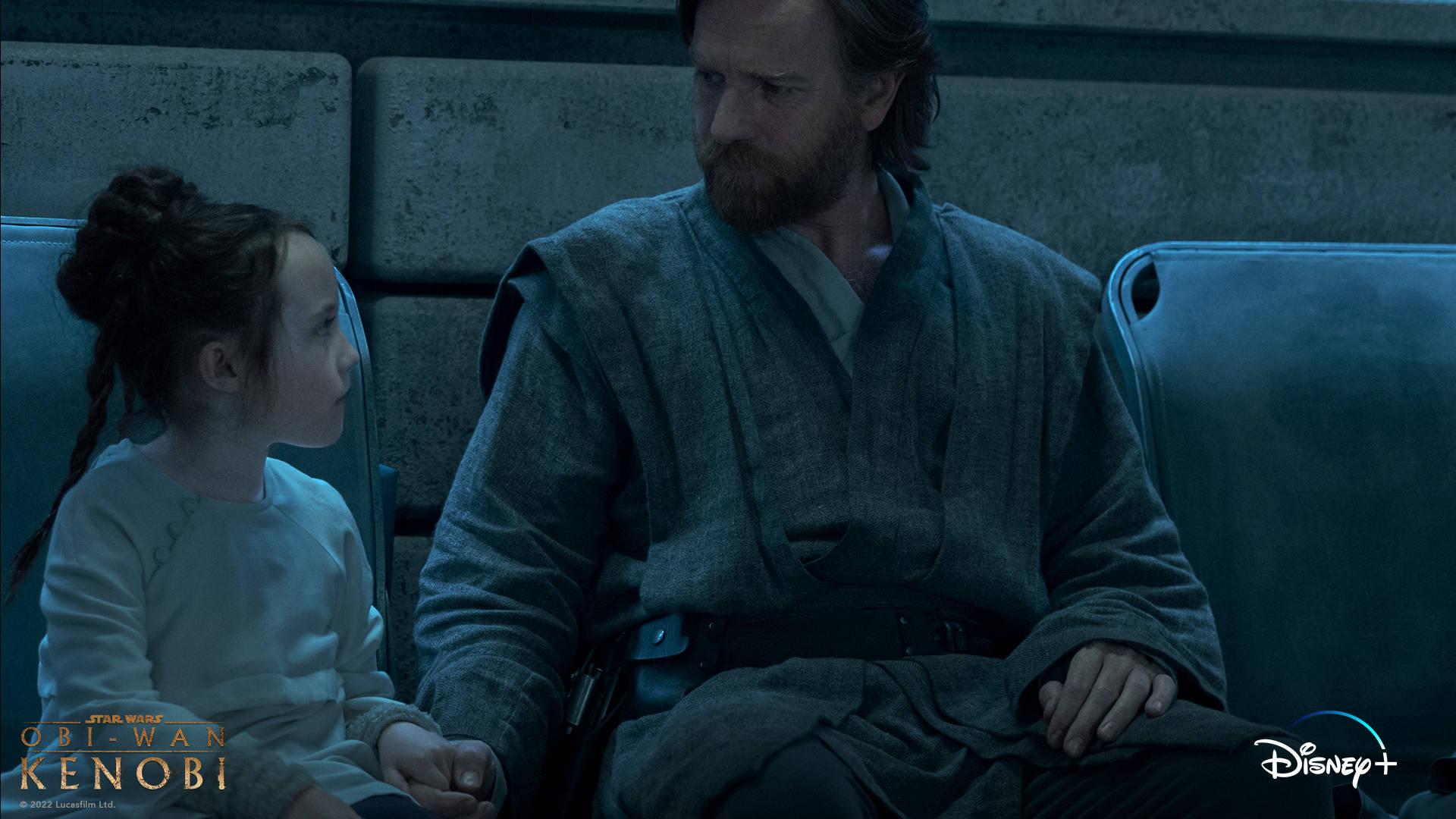 Kenobi 桌布 壁紙 — 一個年輕女孩和一個留鬍子的男人並排坐在昏暗的藍色燈光座位上，表情莊嚴地握著手。