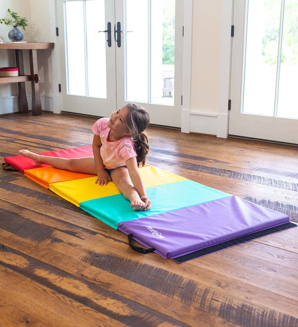 Gymnastics Mat 桌布 壁紙 — 一個年輕女孩在明亮的陽光房間裡，在鋪在硬木地板上的彩虹色體操墊上伸展身體。
