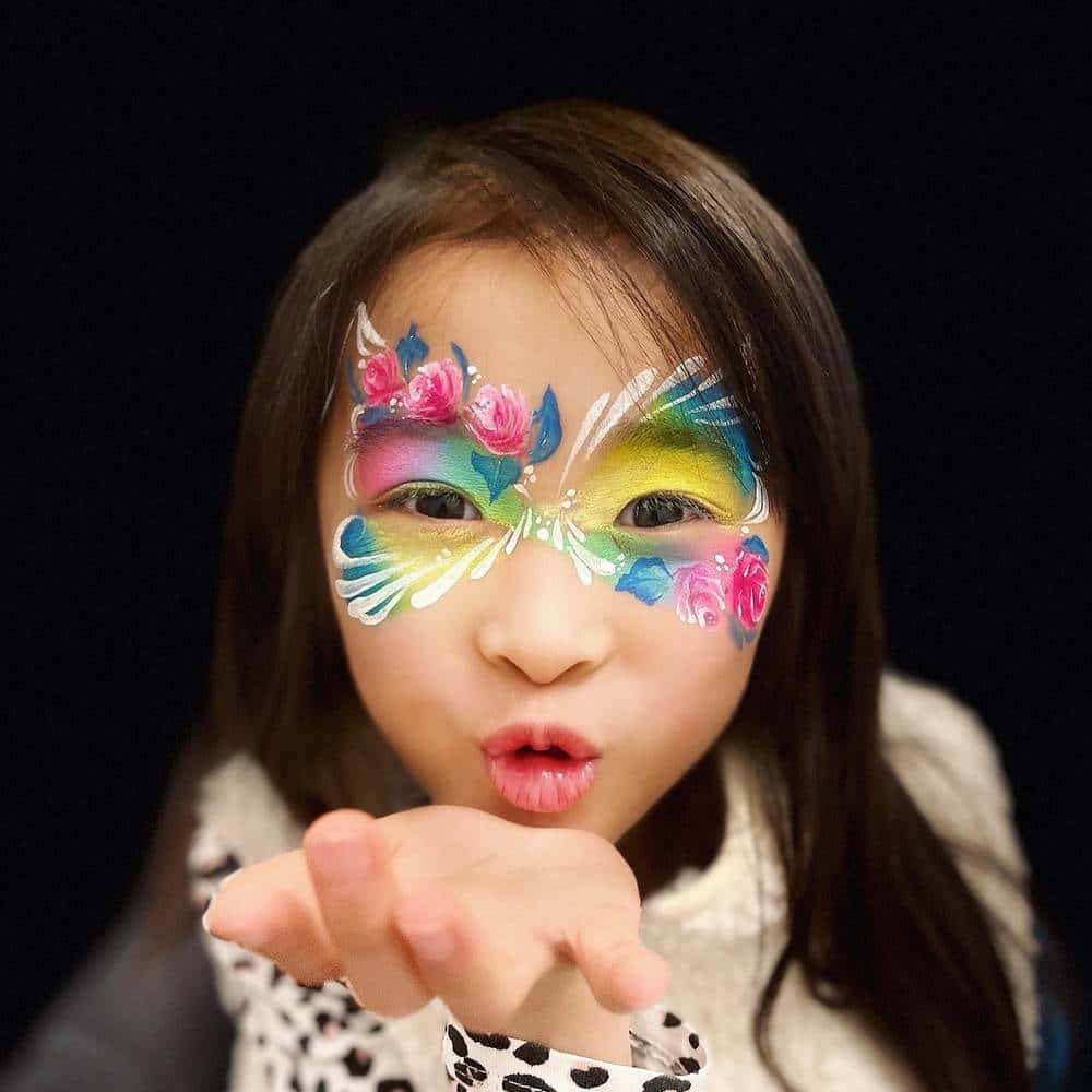Butterfly Face Painting 桌布 壁紙 — 一個年輕女孩在黑色背景下，帶有鮮豔的蝴蝶和玫瑰臉部彩繪，正在飛吻。