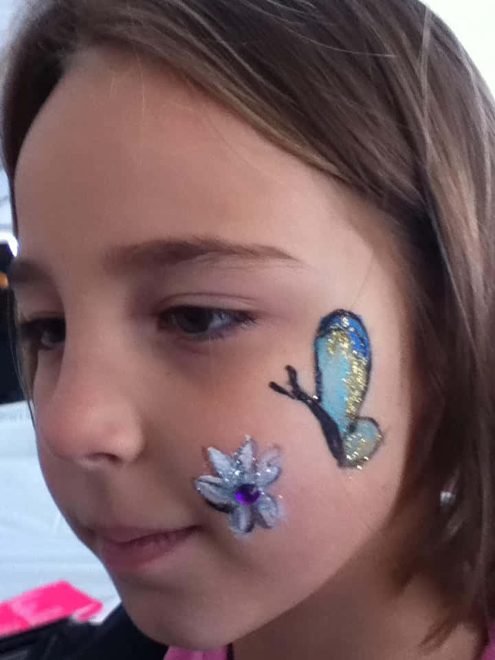 Butterfly Face Painting 桌布 壁紙 — 一個年輕女孩的臉頰上裝飾著閃亮的藍色蝴蝶和銀色花朵臉部彩繪。