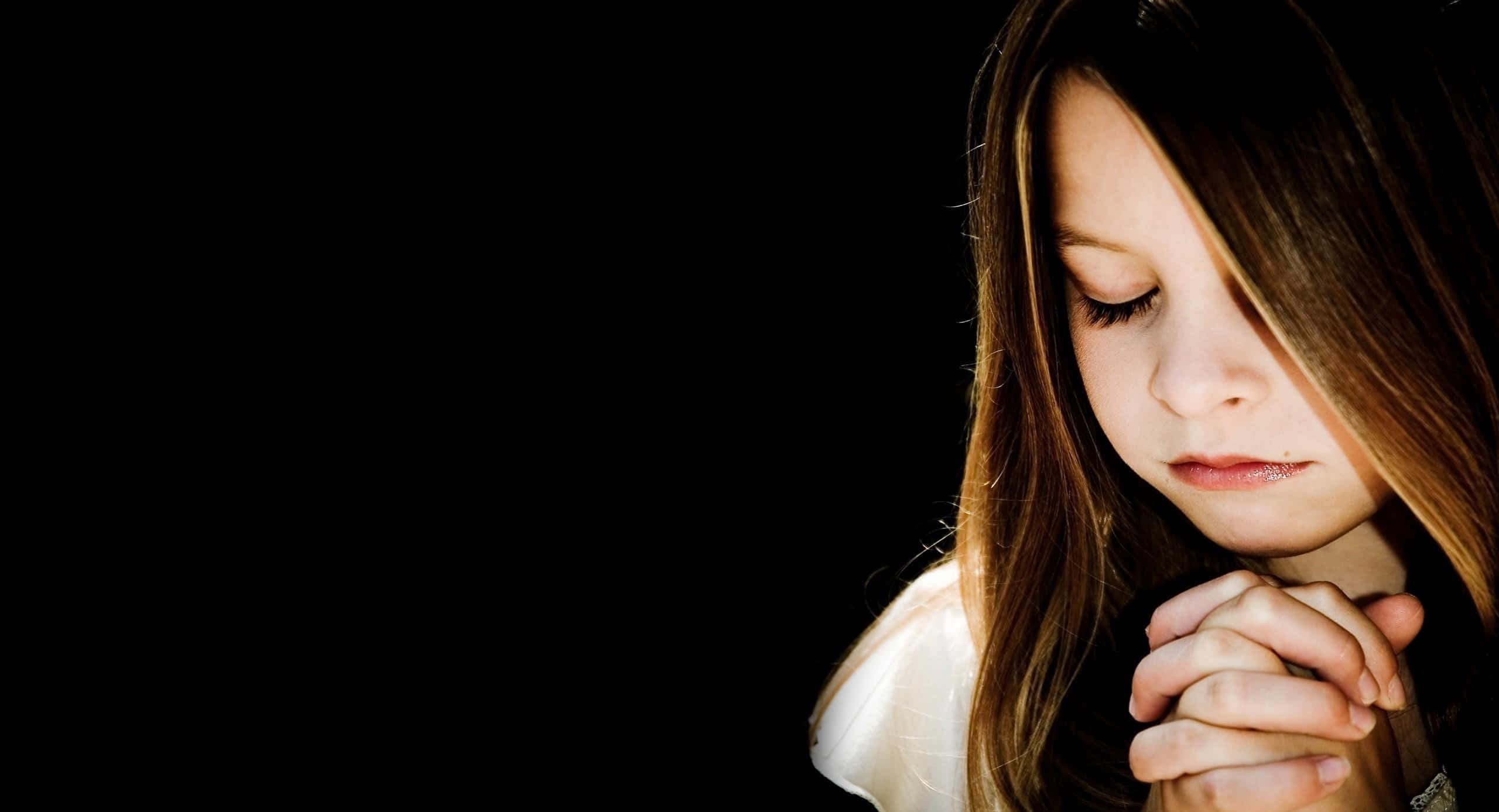 Prayer 桌布 壁紙 — 一個年輕女孩閉上眼睛，雙手合十，在純黑背景前祈禱。