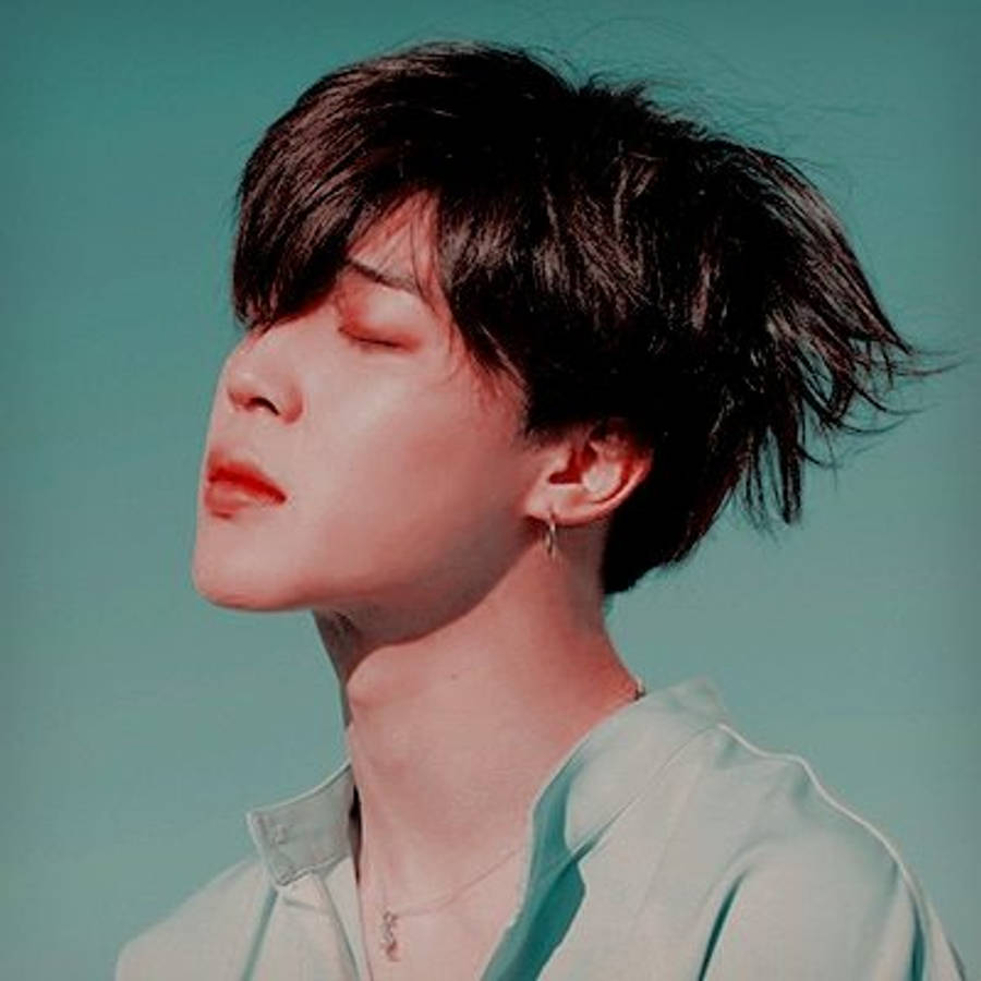 Bts Jimin 桌布 壁紙 — 一個年輕男子，一頭凌亂的黑髮，在青綠色背景前閉上眼睛，穿著淺色襯衫和精緻的珠寶。