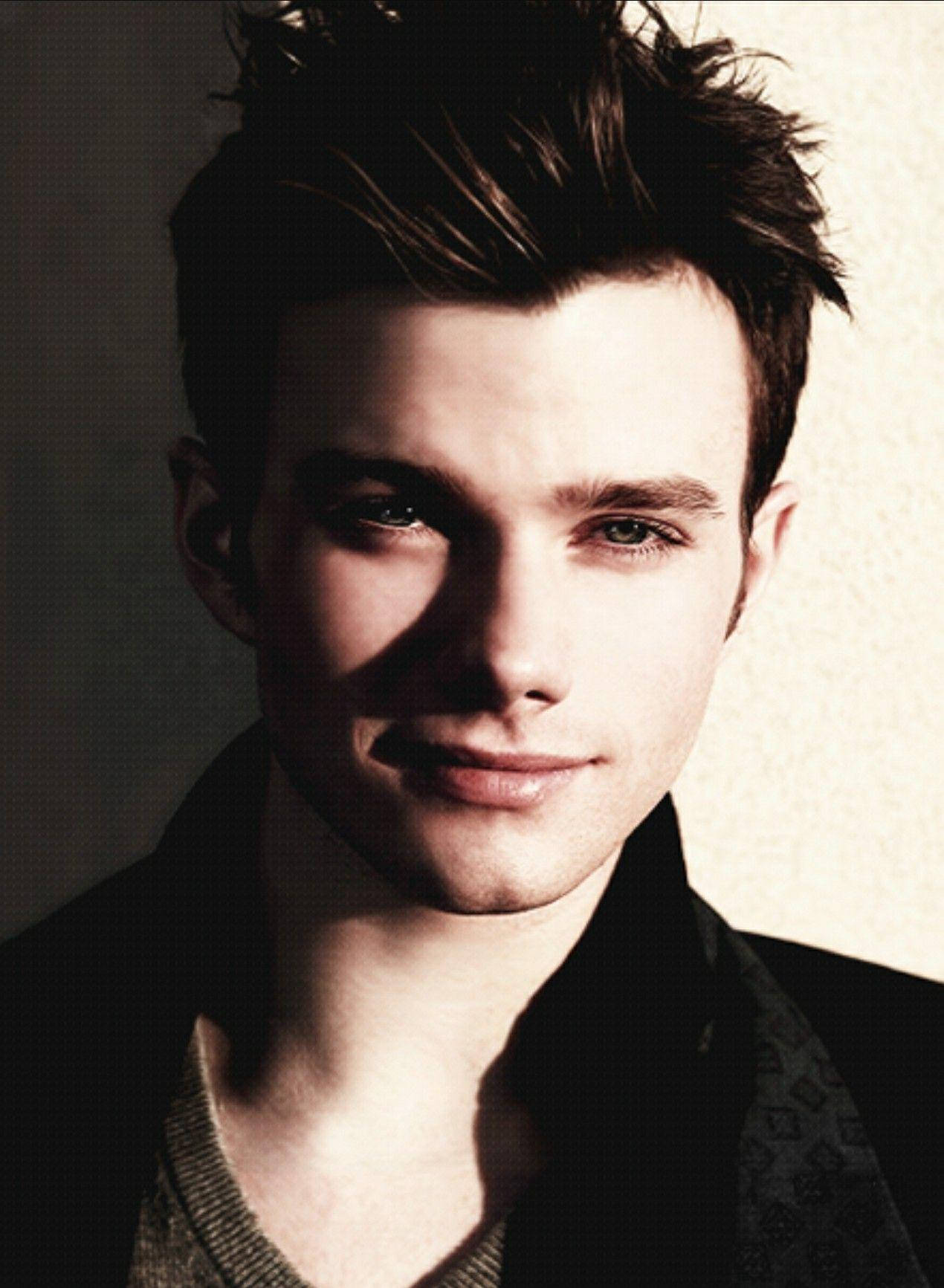 Chris Colfer 桌布 壁紙 — 一個年輕男子，一頭凌亂的黑髮，眼神專注，在戲劇性的側光下直視鏡頭。